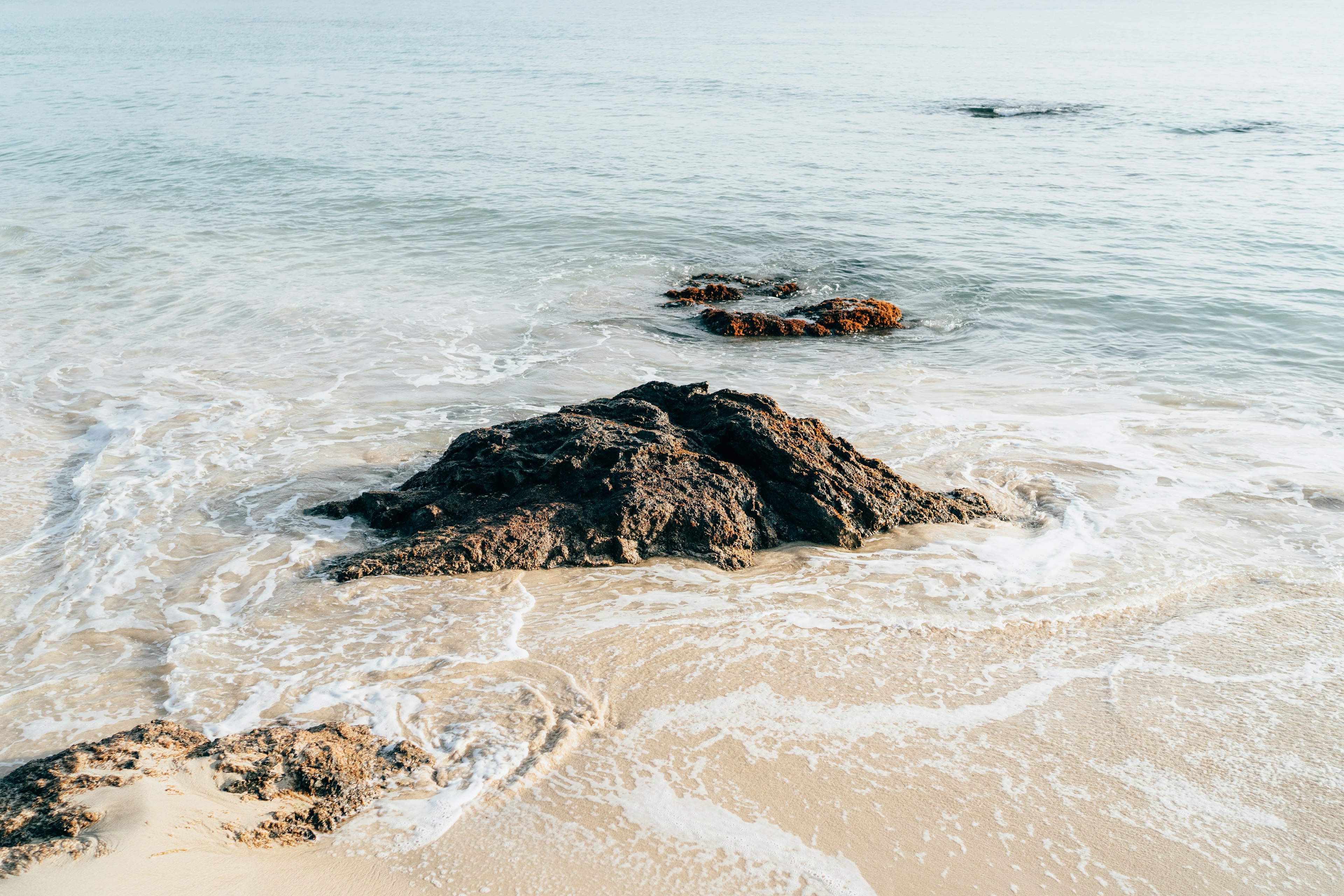 A rocky outcrop partially submerged in gentle waves on a sandy beach