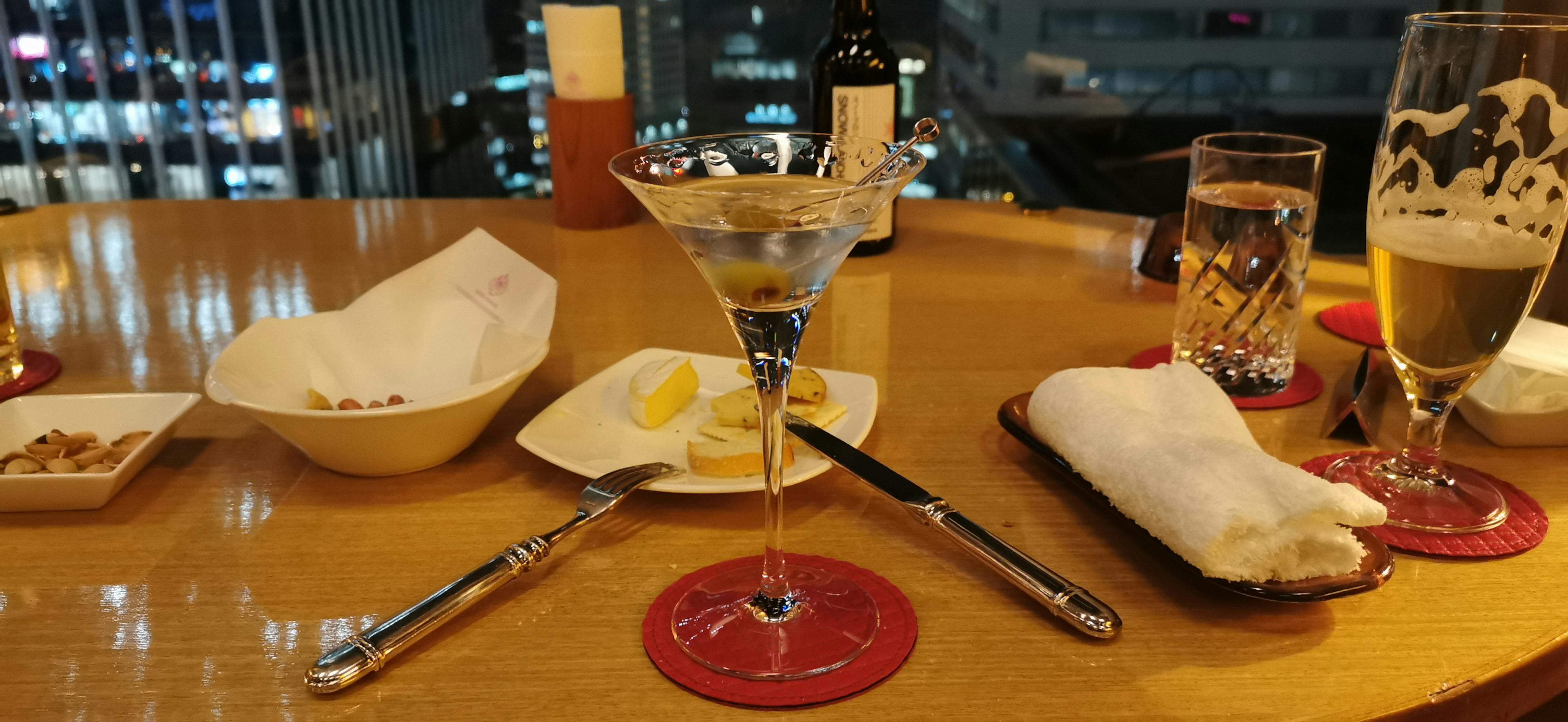 Cocktail and snacks on a bar table with a city view at night