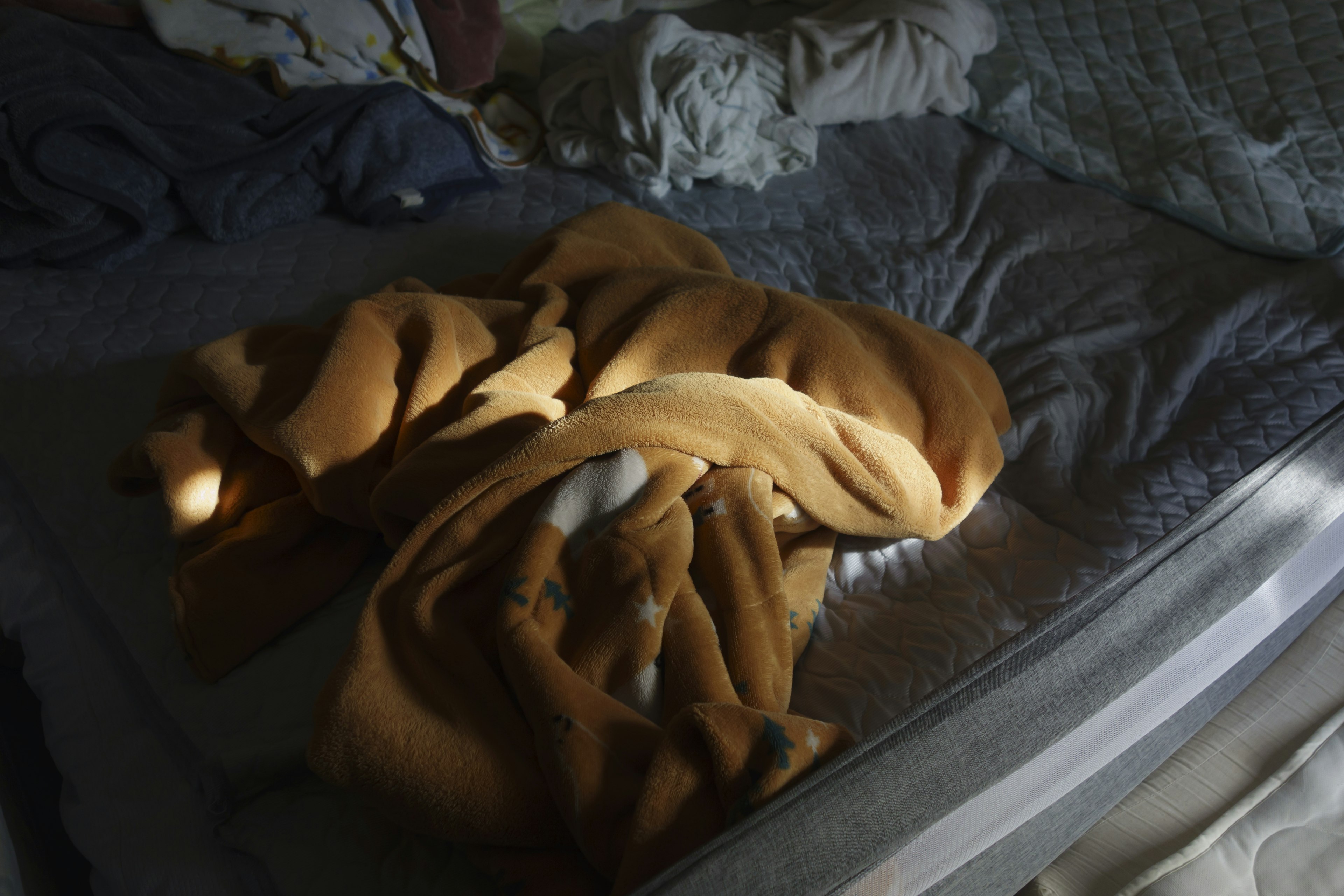 An orange blanket crumpled on a bed in a dimly lit room