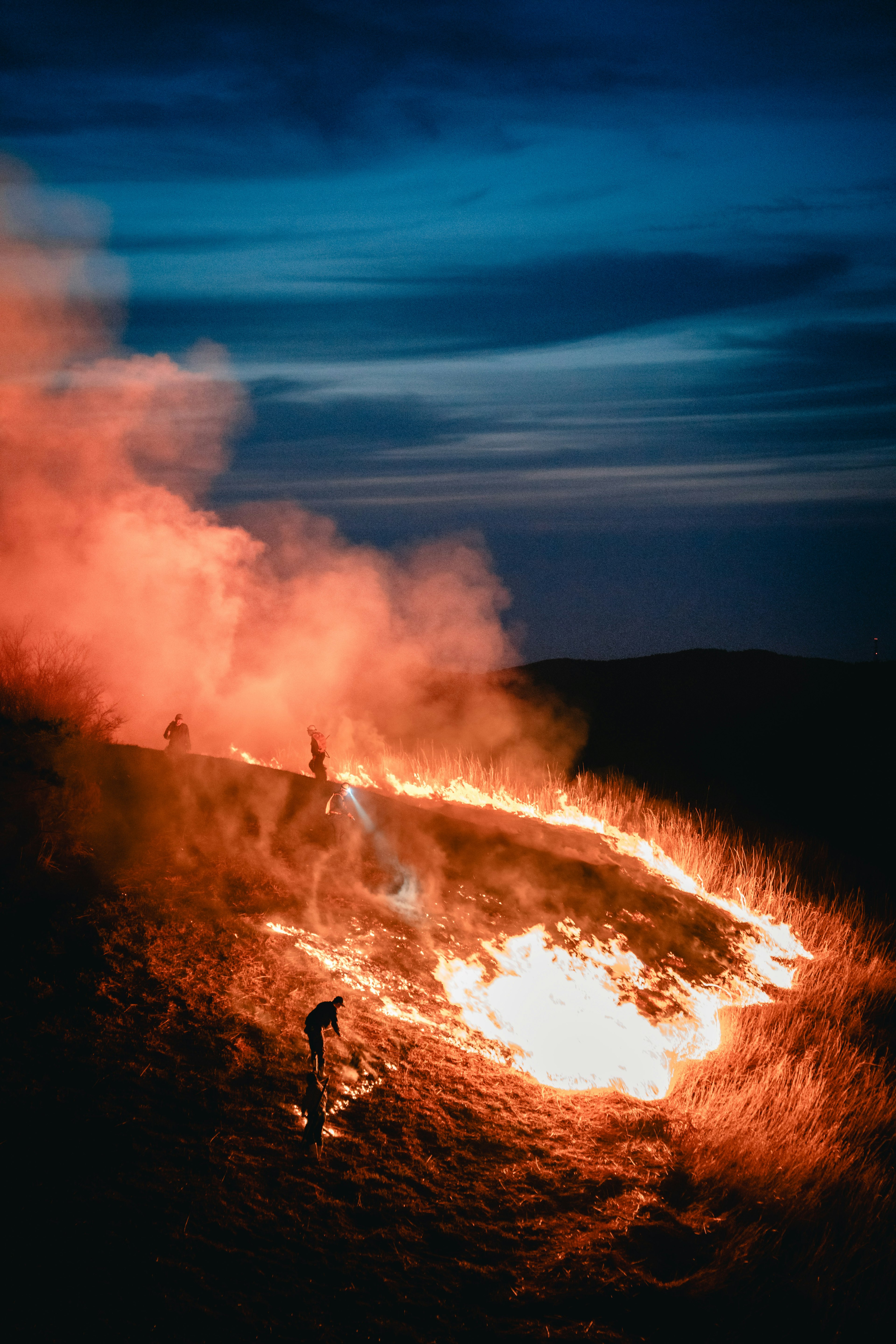 Un paisaje de llamas y humo en una colina durante el crepúsculo