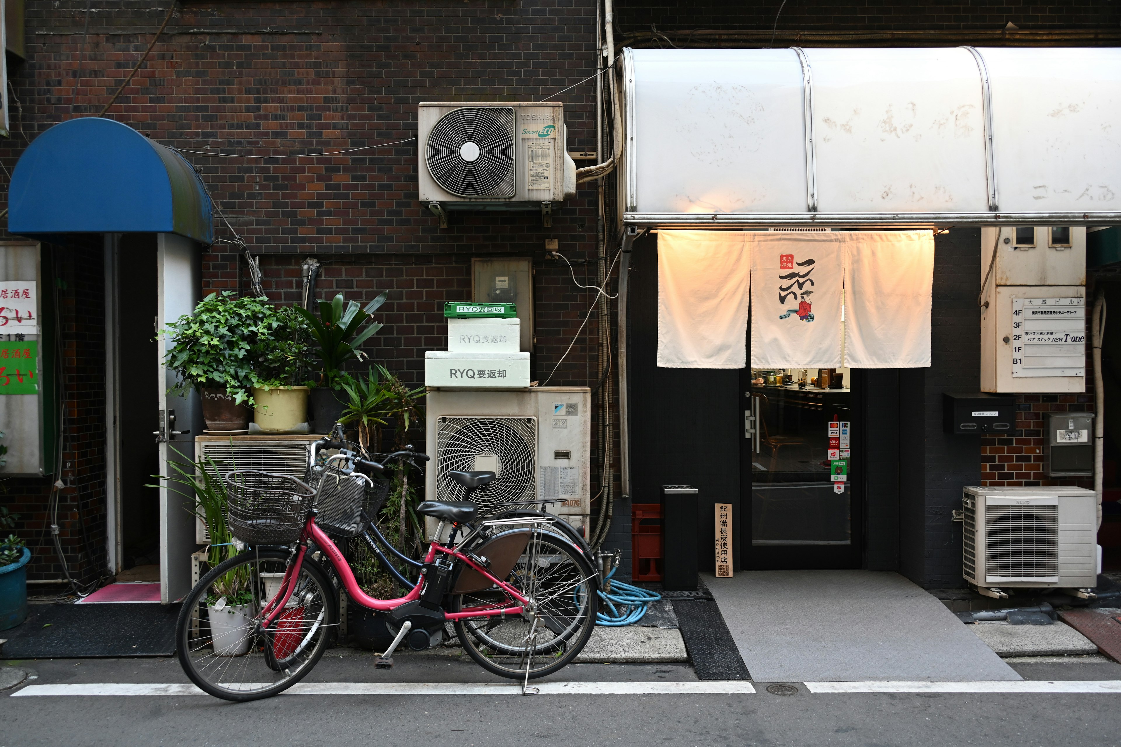 赤い自転車が置かれた日本の飲食店の外観 植物やエアコンが見える