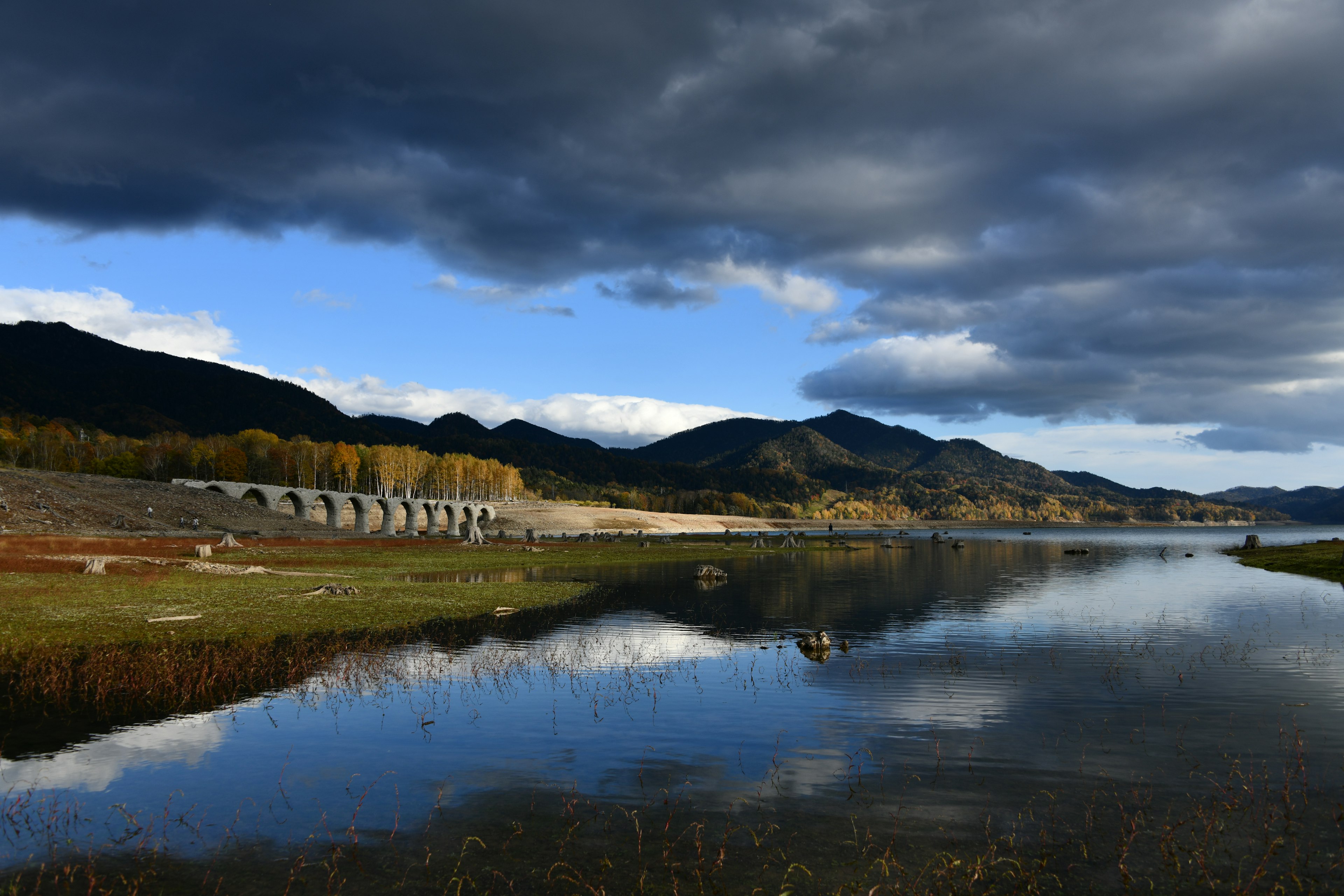 Beautiful natural landscape with a calm river mountains cloudy sky reflecting water surface autumn trees