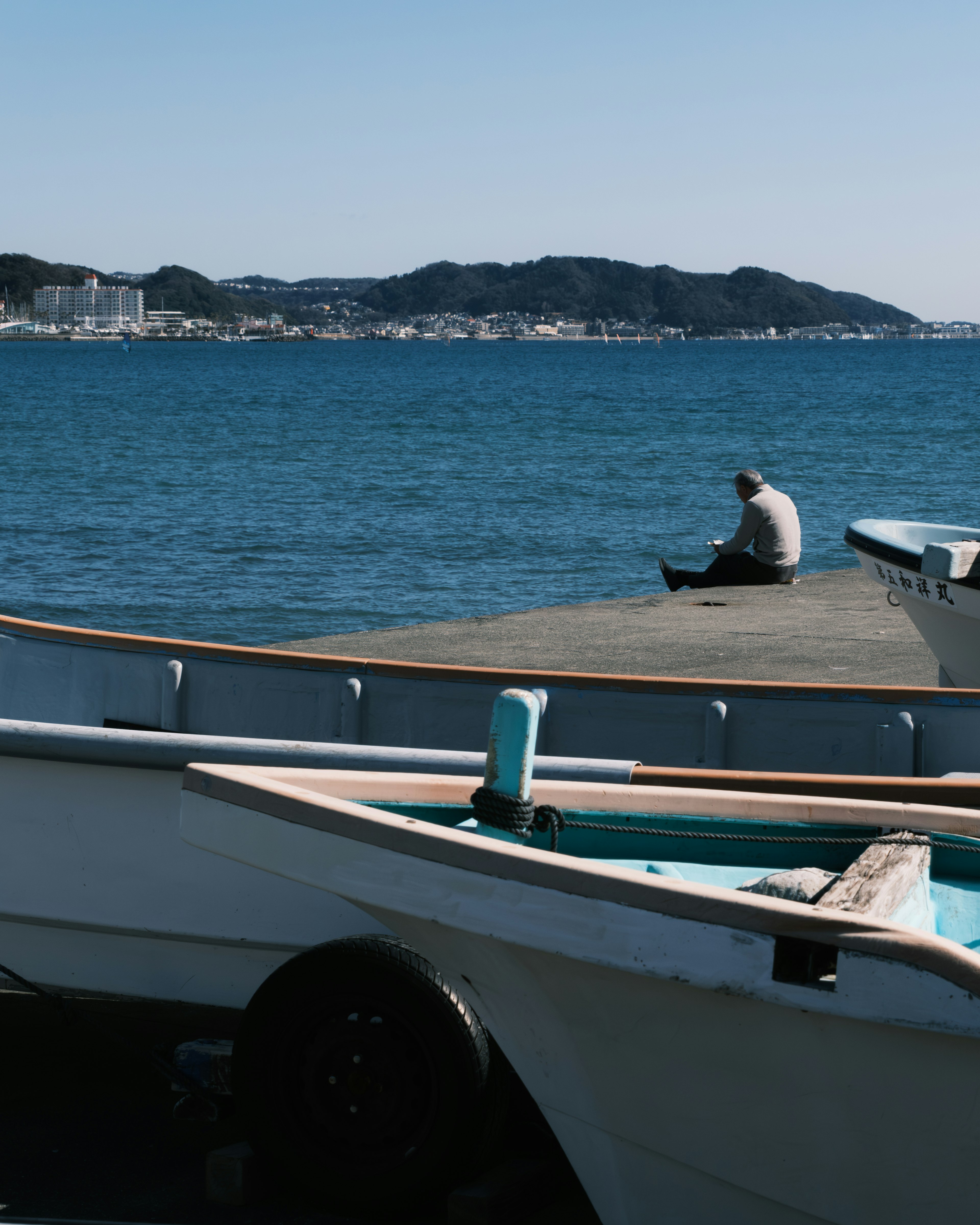 A man sitting peacefully by the sea with small boats in the foreground