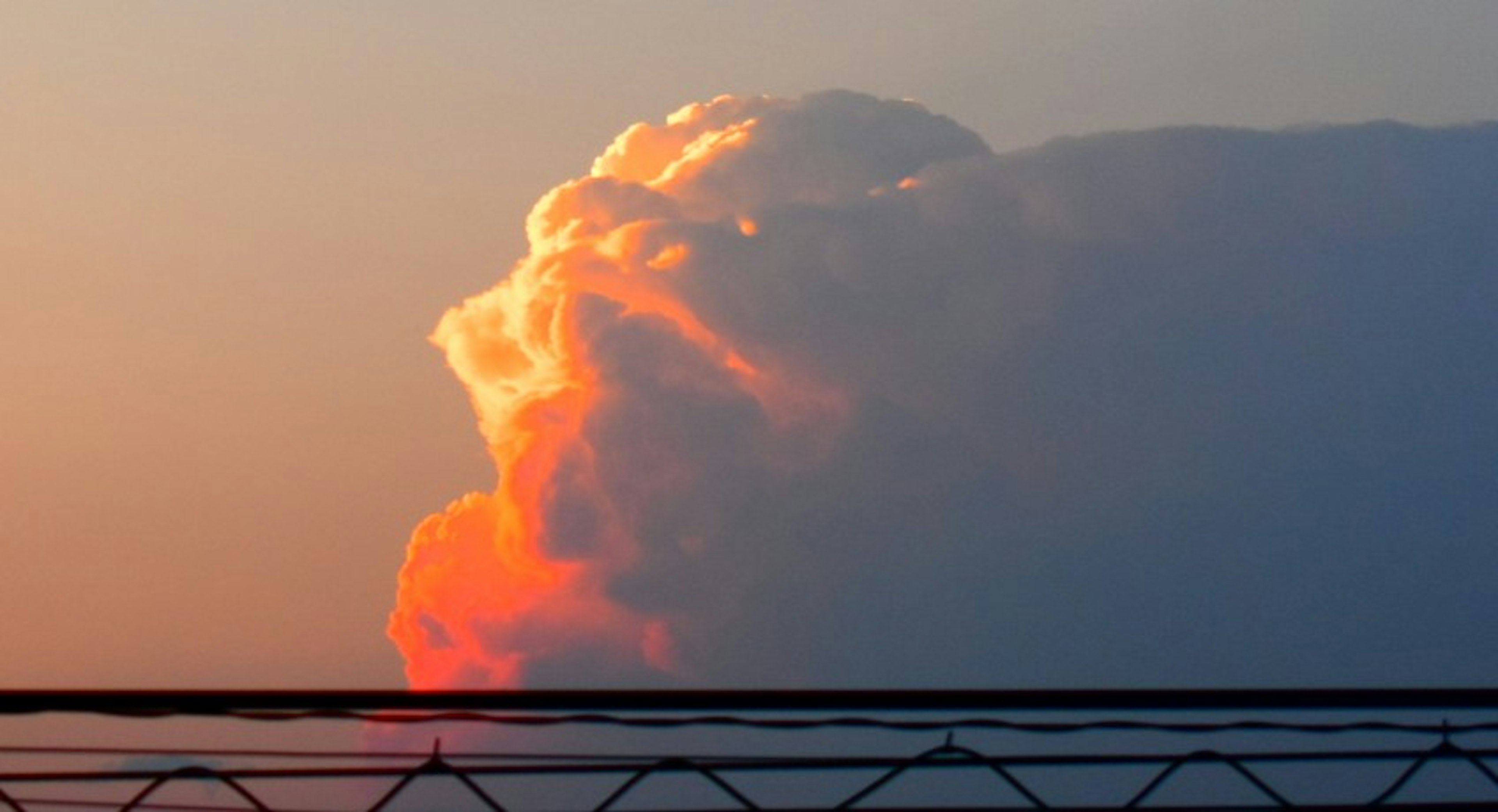 夕焼けの空に浮かぶオレンジ色の雲の塊とその下に見えるフェンス