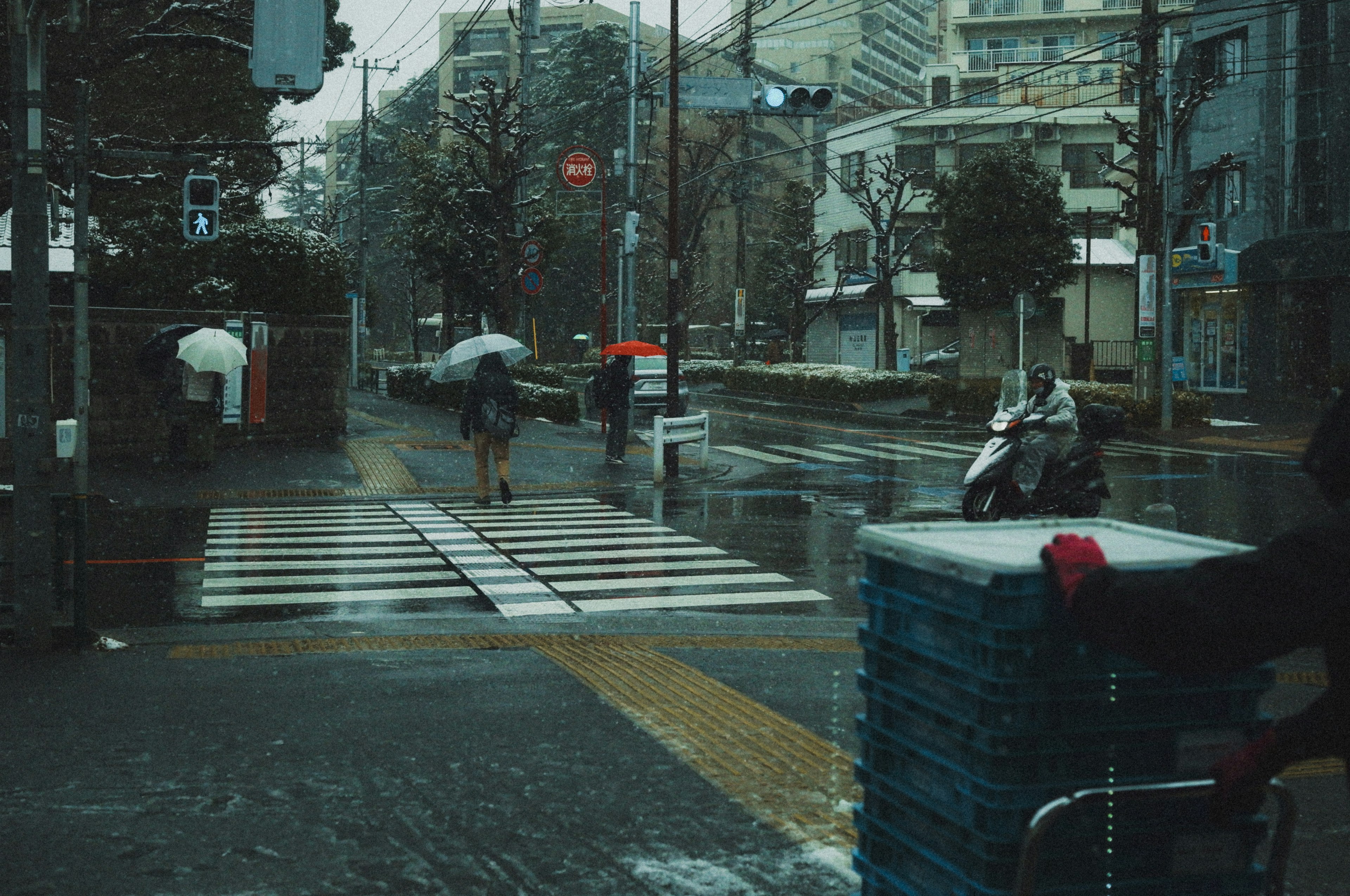 ฉากเมืองที่มีคนถือร่มและมอเตอร์ไซค์ที่ทางม้าลายในฝนตก