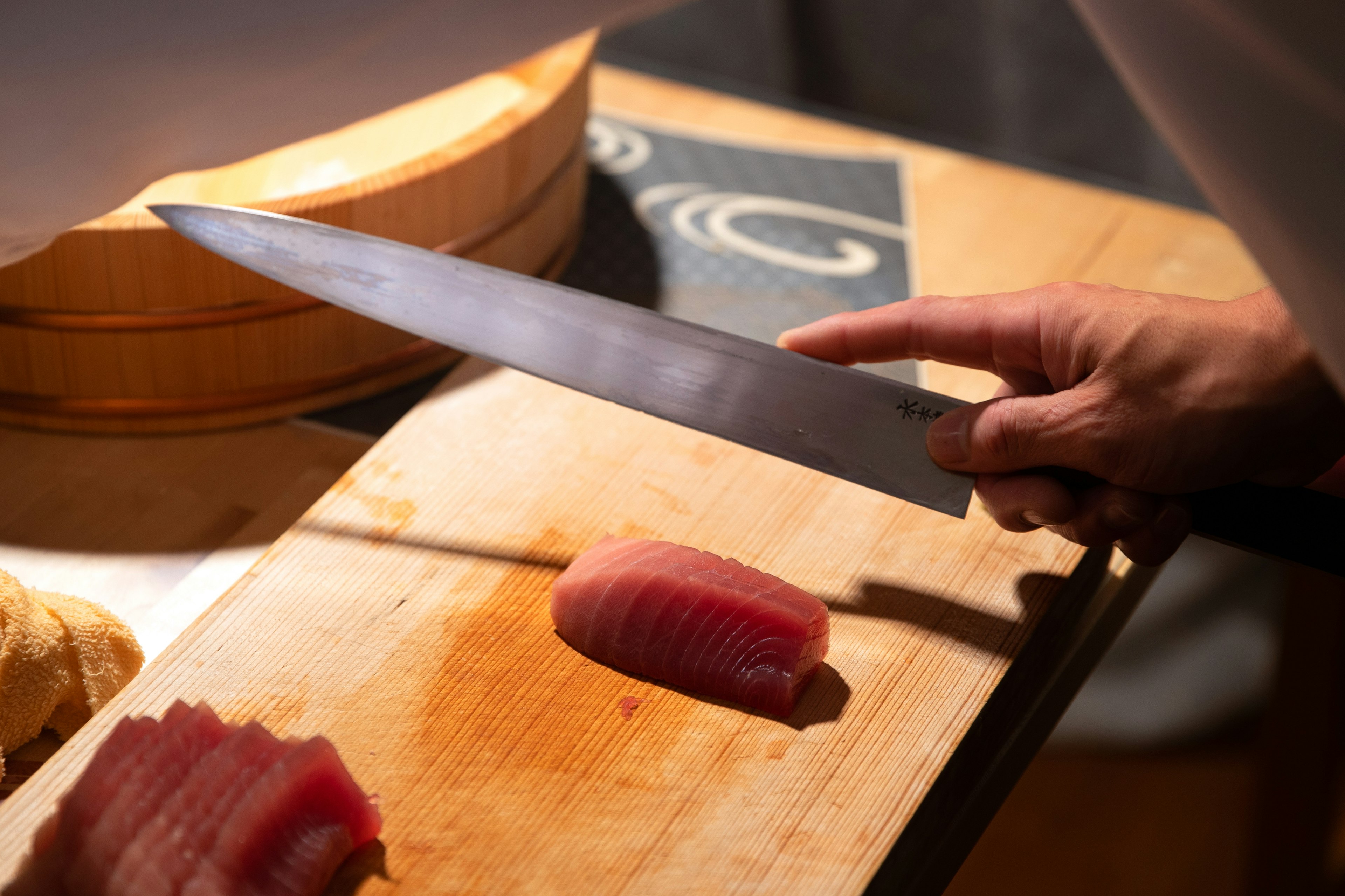 Mano di chef con un coltello che affetta sashimi di tonno