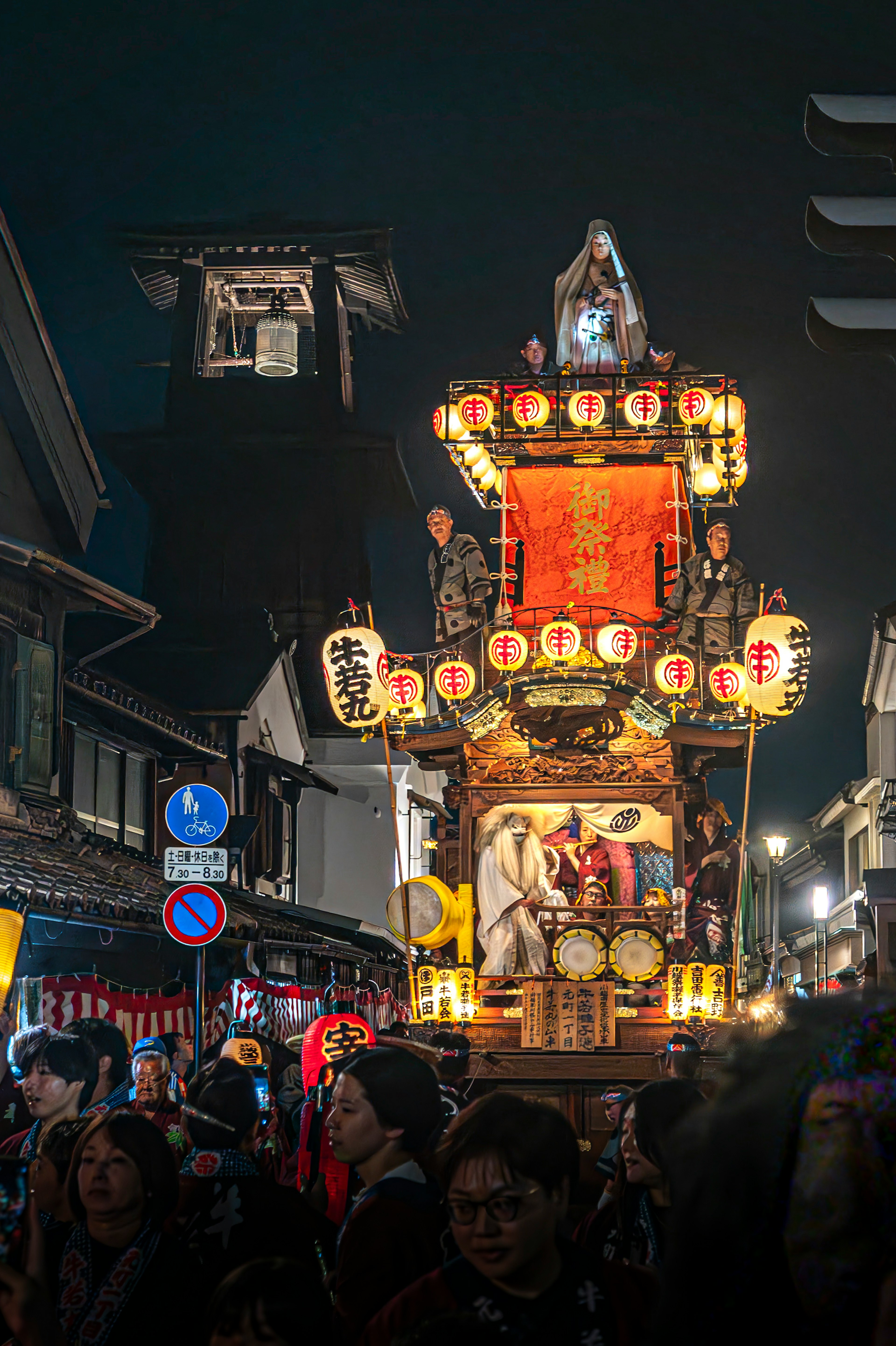 夜の祭りの山車が通りを進む様子を捉えた画像