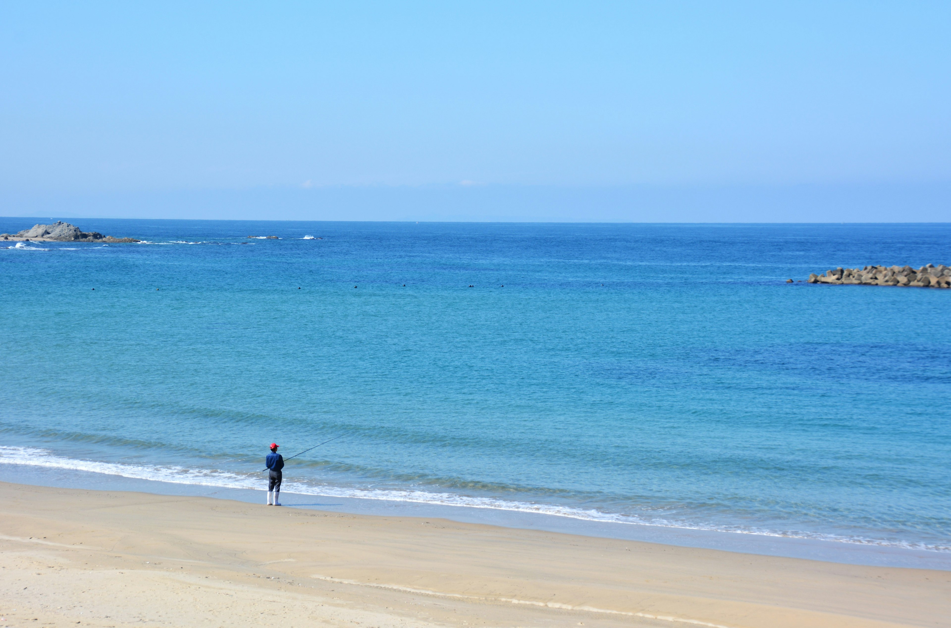 Person steht am Sandstrand mit blauem Ozean