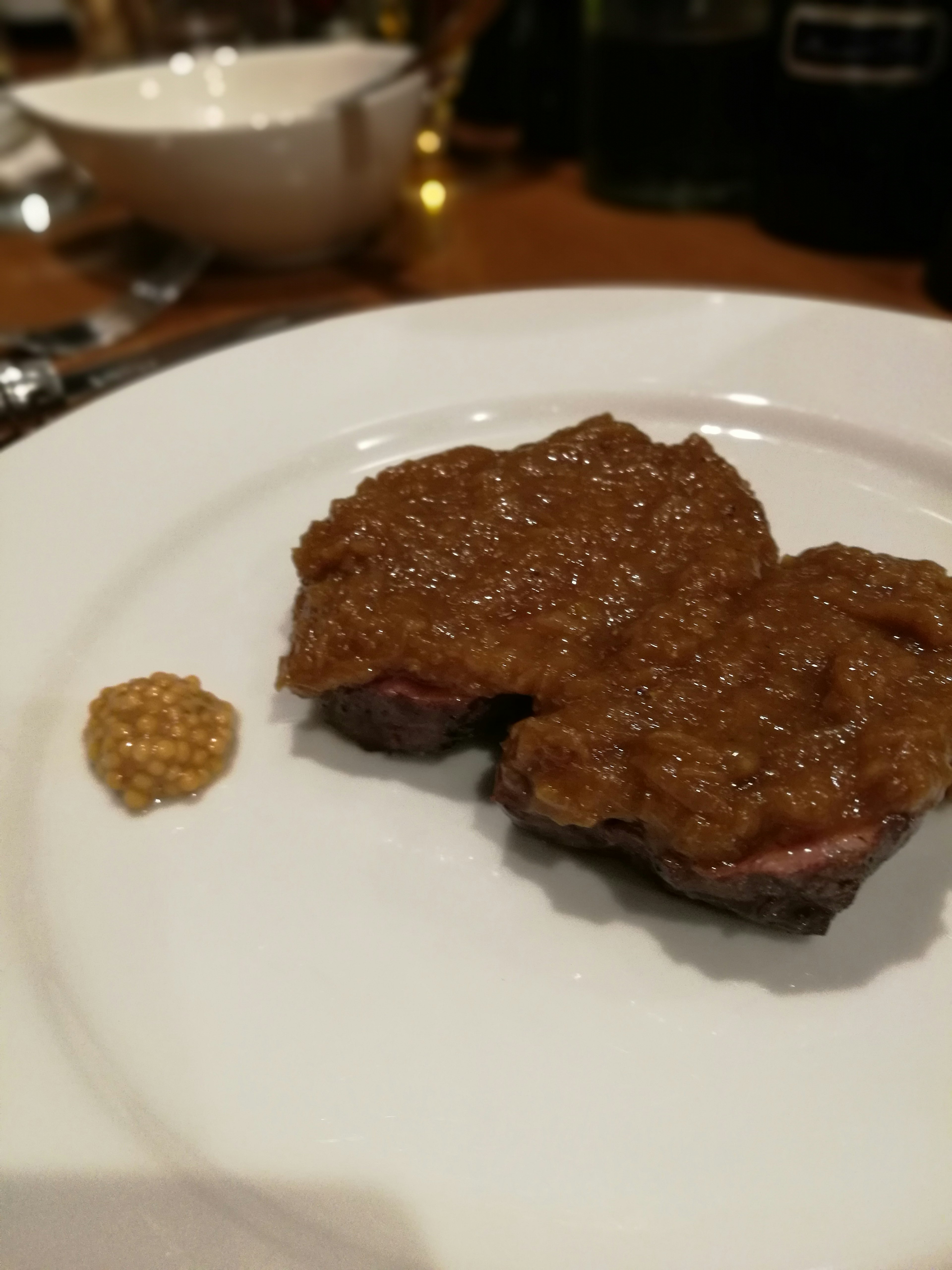 Ein Teller mit einem Fleischgericht, das mit einer reichhaltigen Sauce bedeckt ist, neben einem Klecks Senf