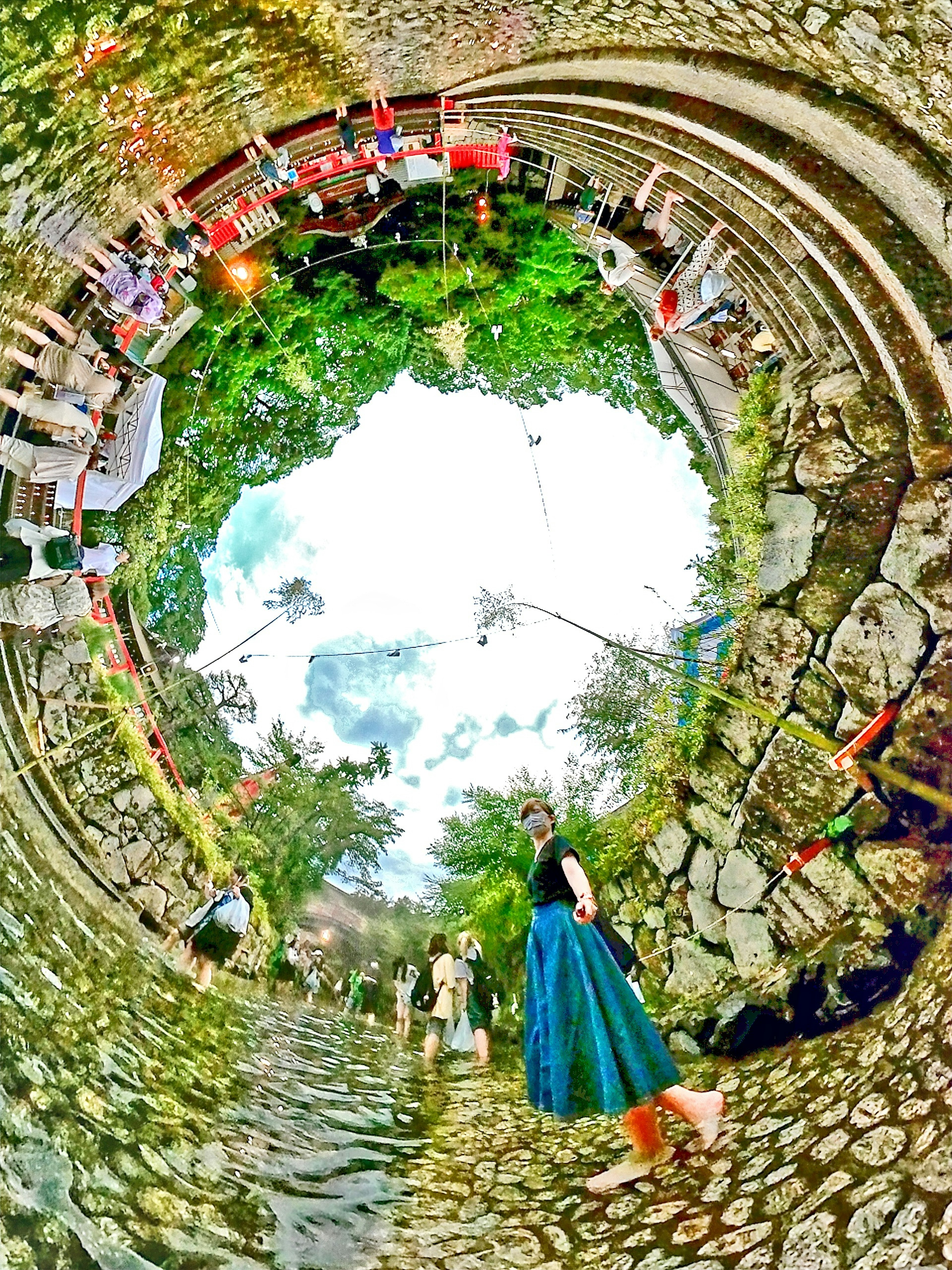 A woman walking on a cobblestone path surrounded by lush greenery and a 360-degree panoramic view