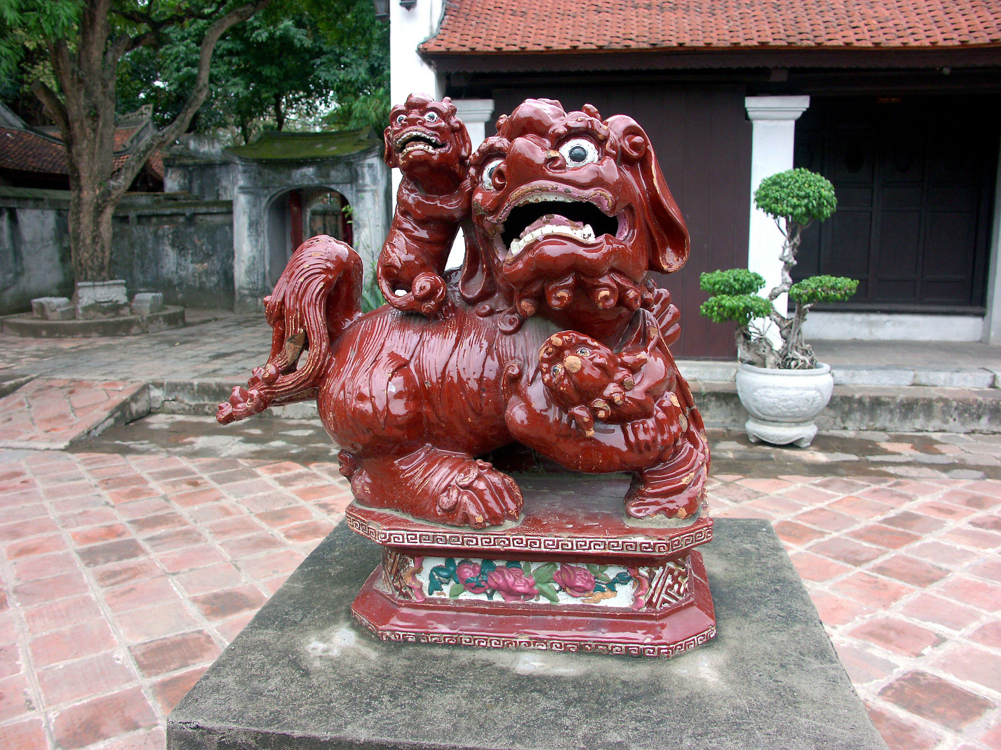 Patung singa merah yang menggendong dua anak singa di halaman