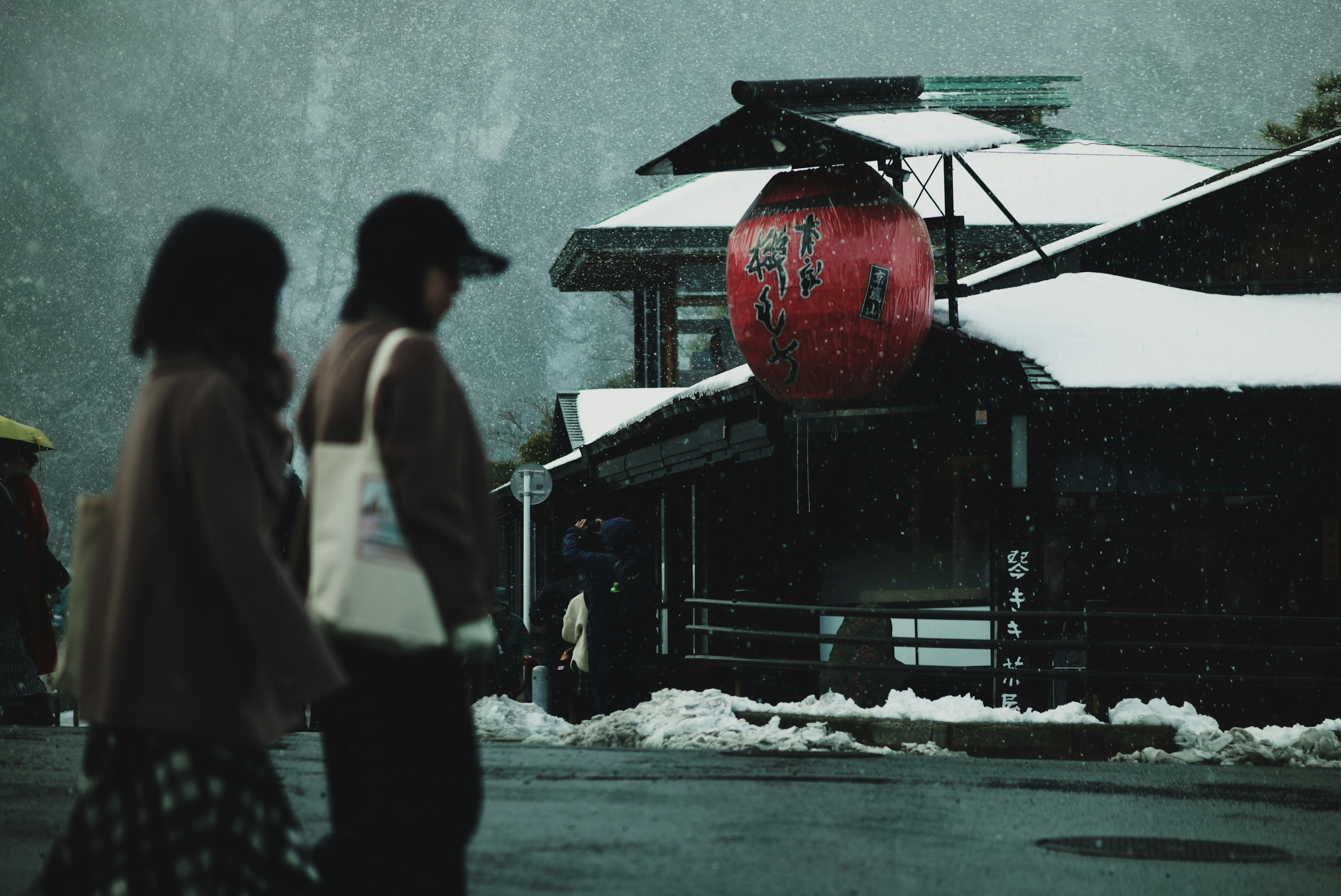 People walking in the snow near a traditional building with a red lantern