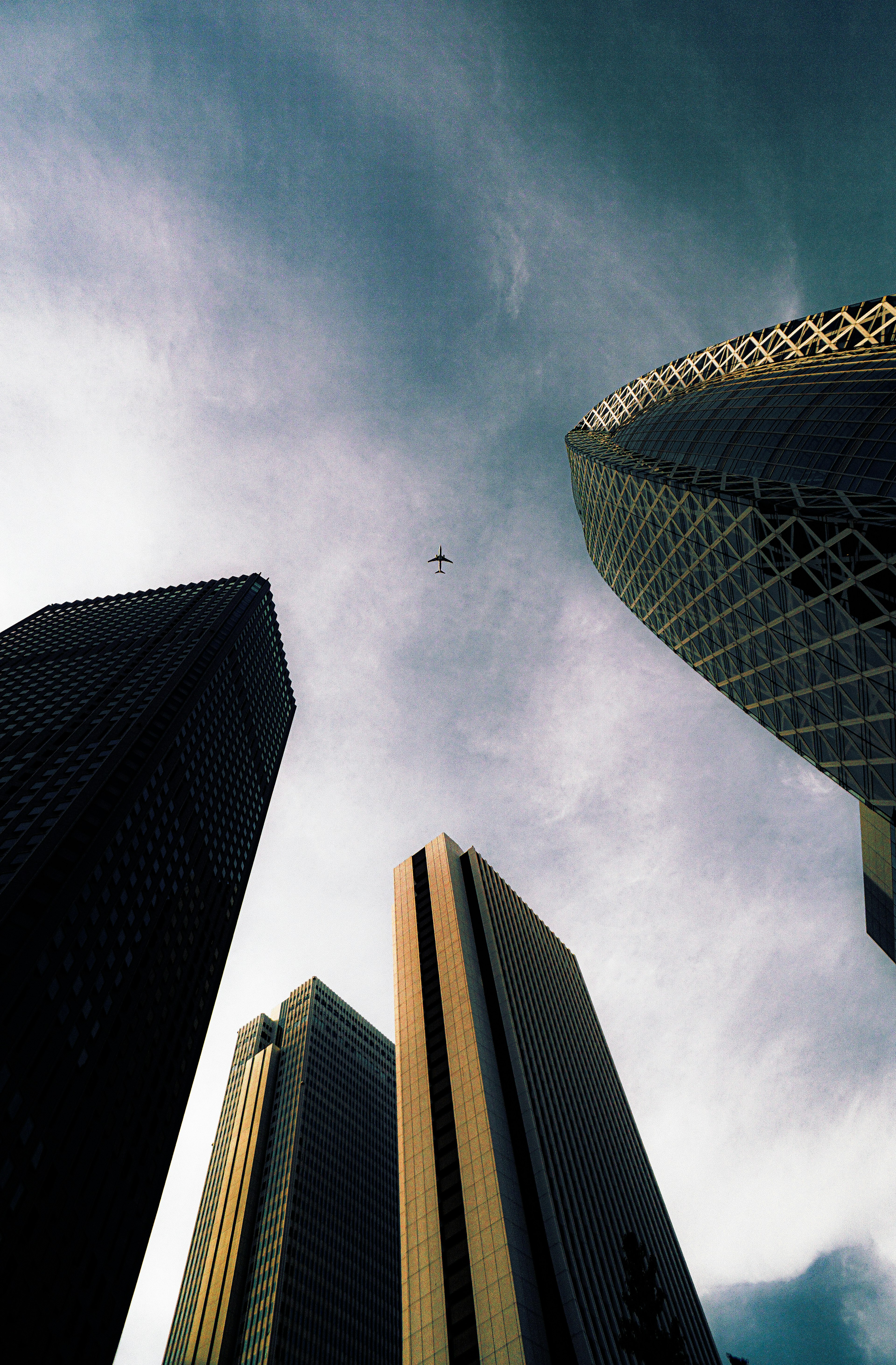 A view looking up at skyscrapers with dramatic cloud patterns and unique architectural designs