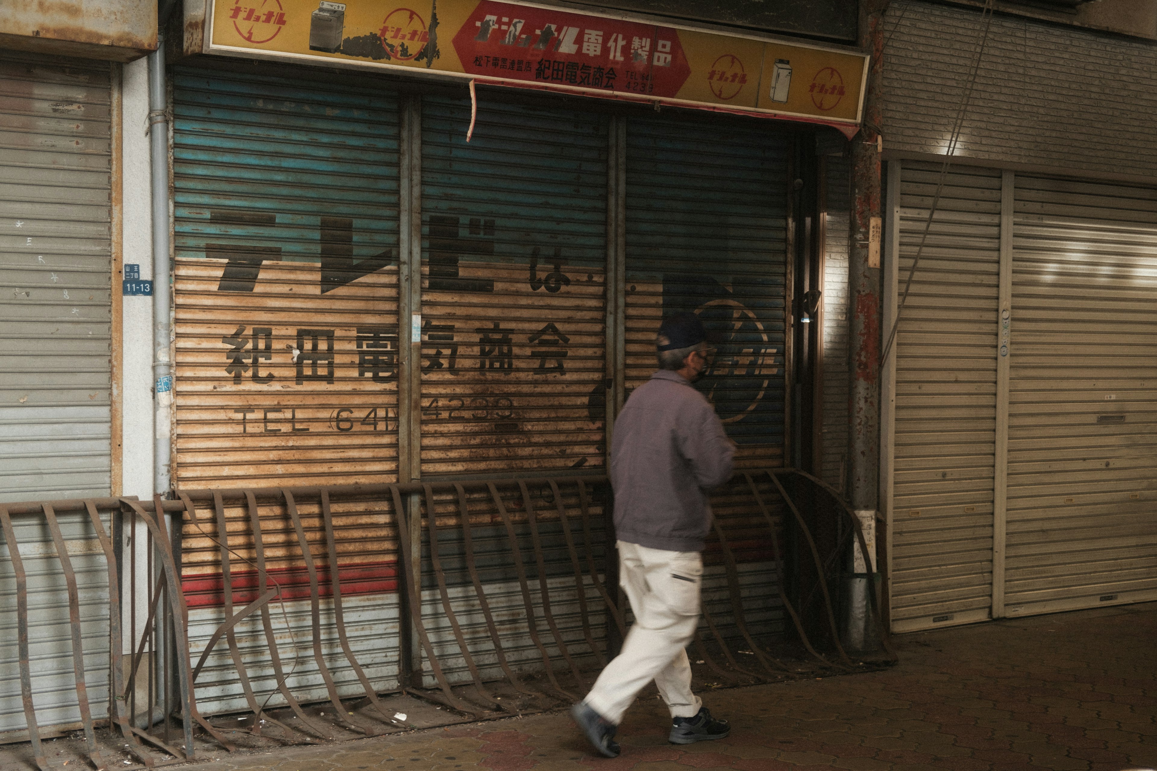 A man walking in front of a shuttered shop at night depicting urban quietness