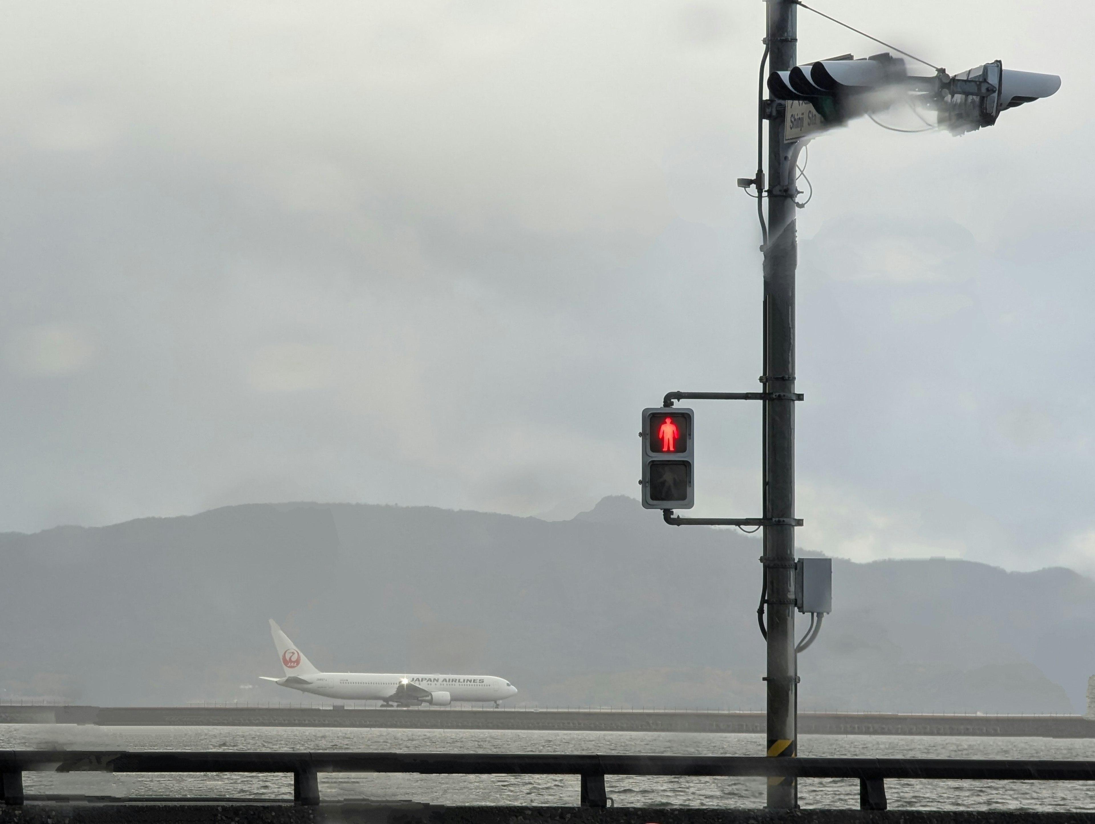 Un aereo che decolla in un tempo nebbioso con un semaforo rosso visibile nelle vicinanze e un cielo nuvoloso