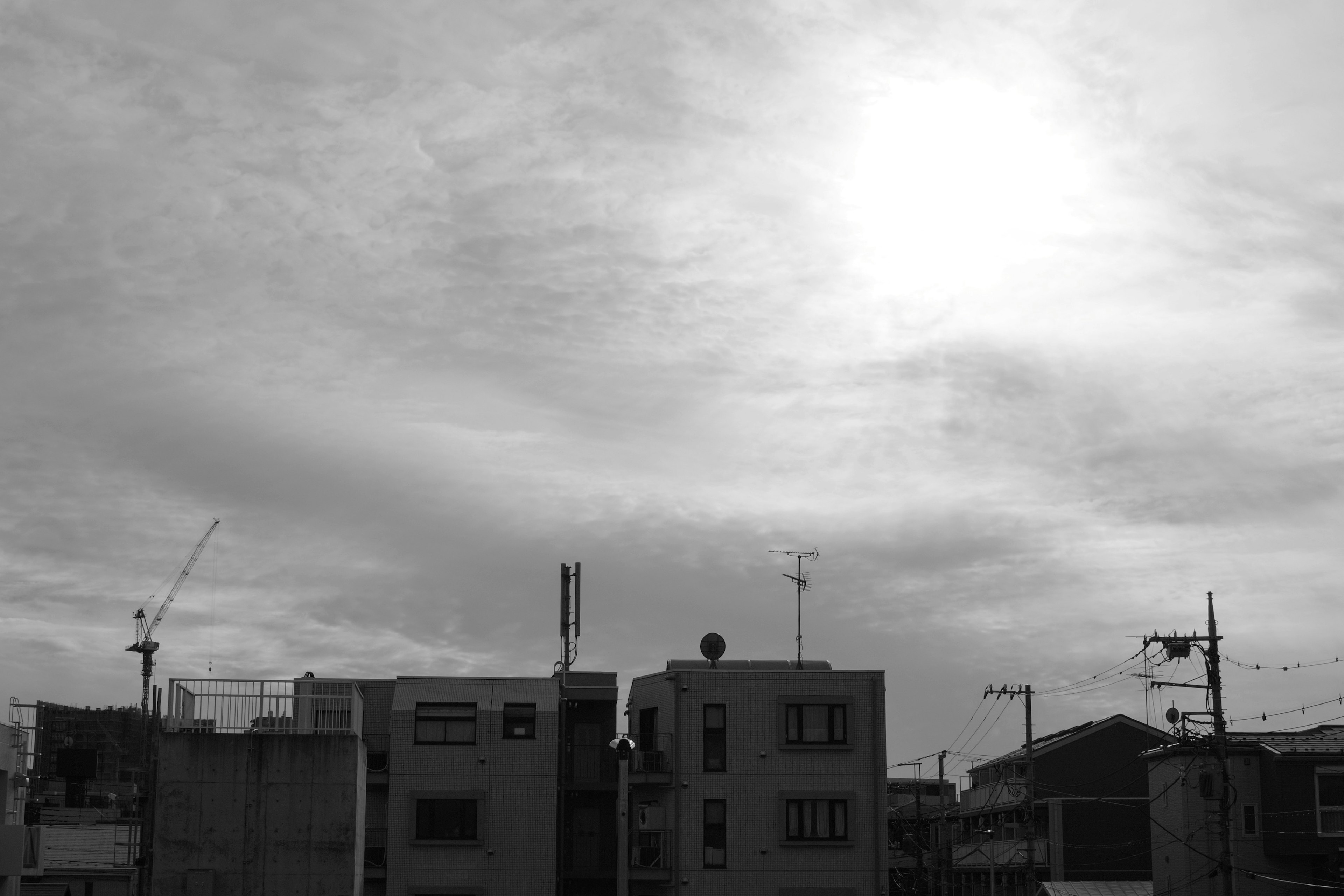 白黒の都市風景に広がる雲と太陽