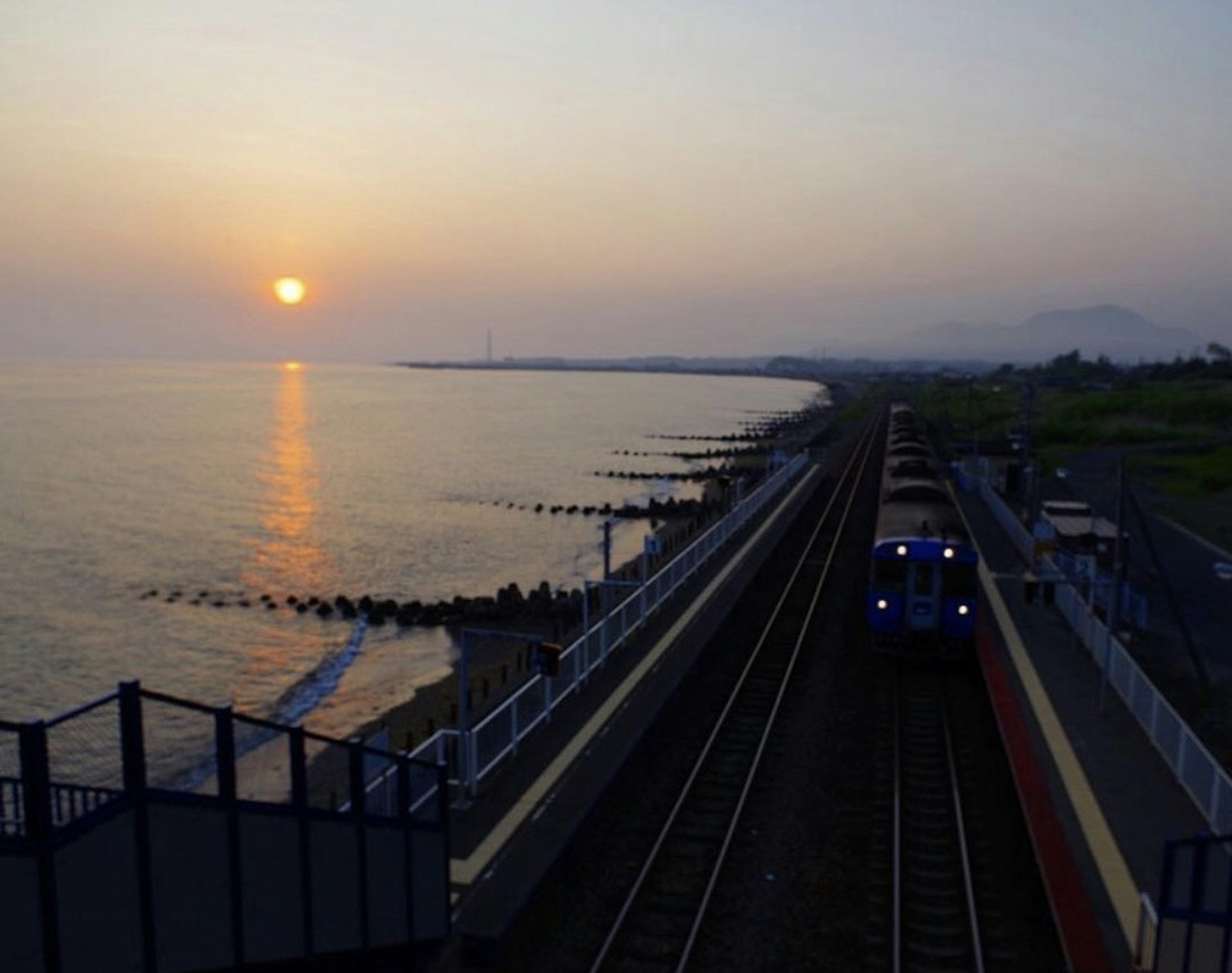 夕日が海に沈む様子と沿岸の鉄道