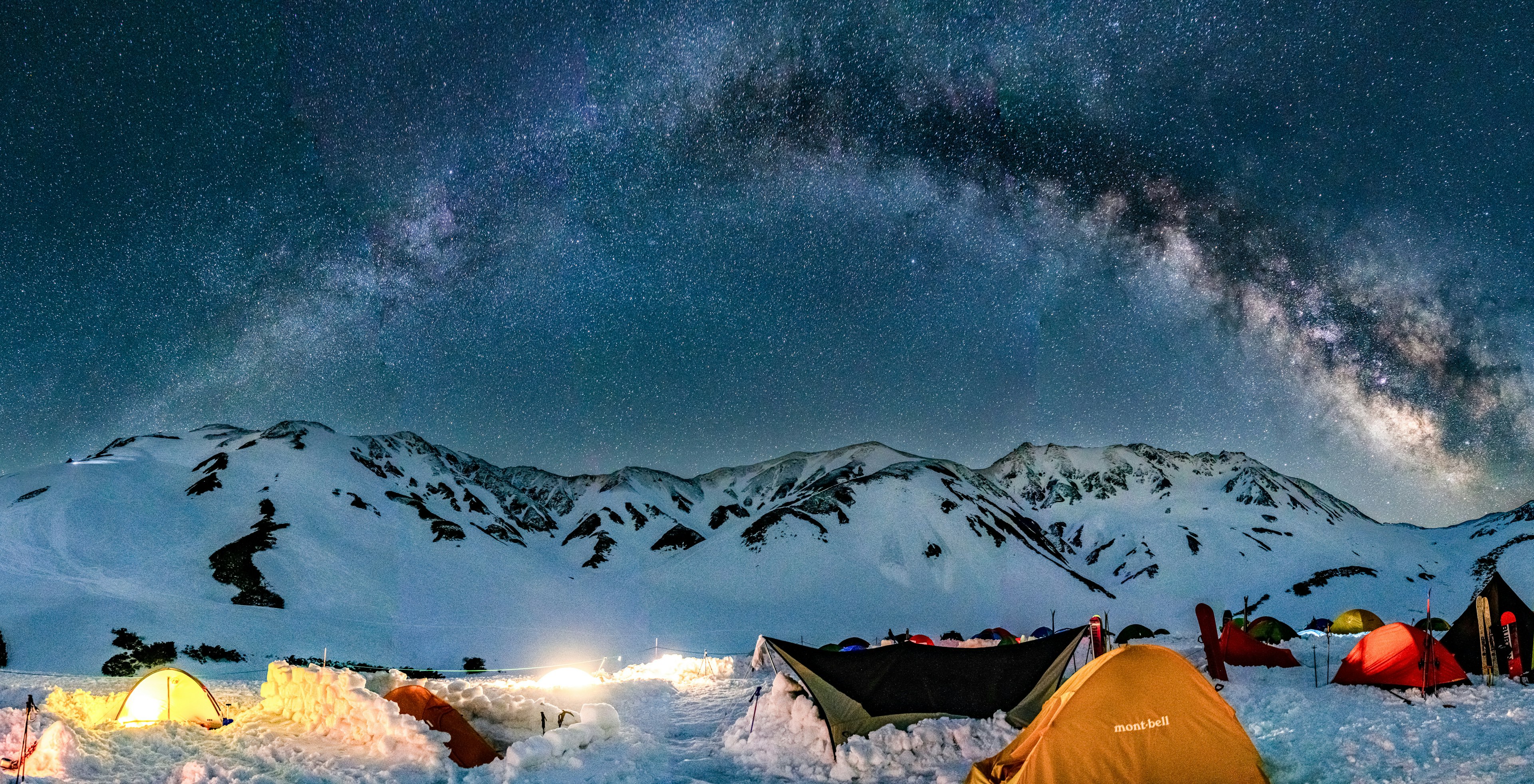 Campingplatz in den verschneiten Bergen unter einem Sternenhimmel mit einem Galaxienbogen