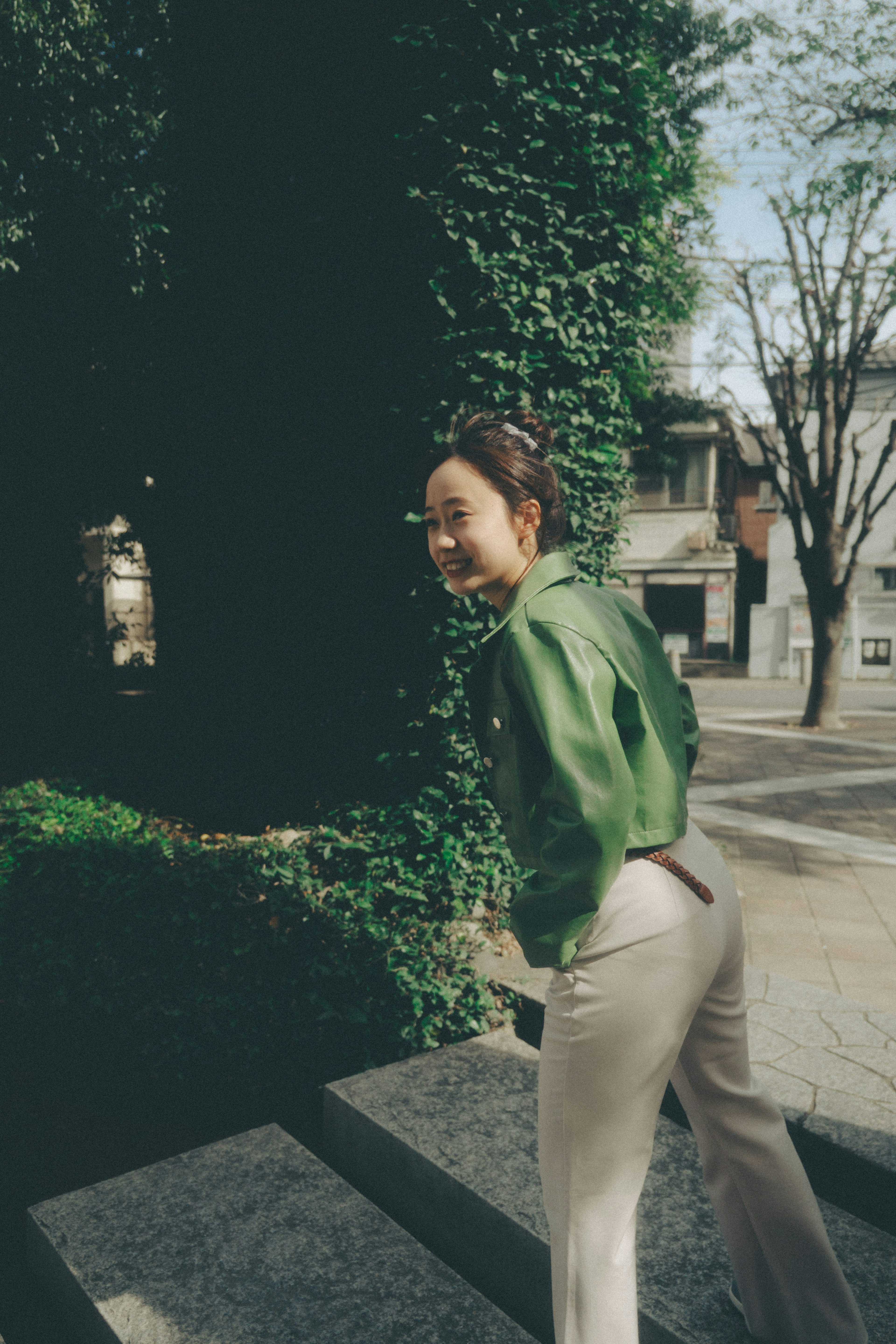 Mujer con chaqueta verde sonriendo y girándose con vegetación de fondo