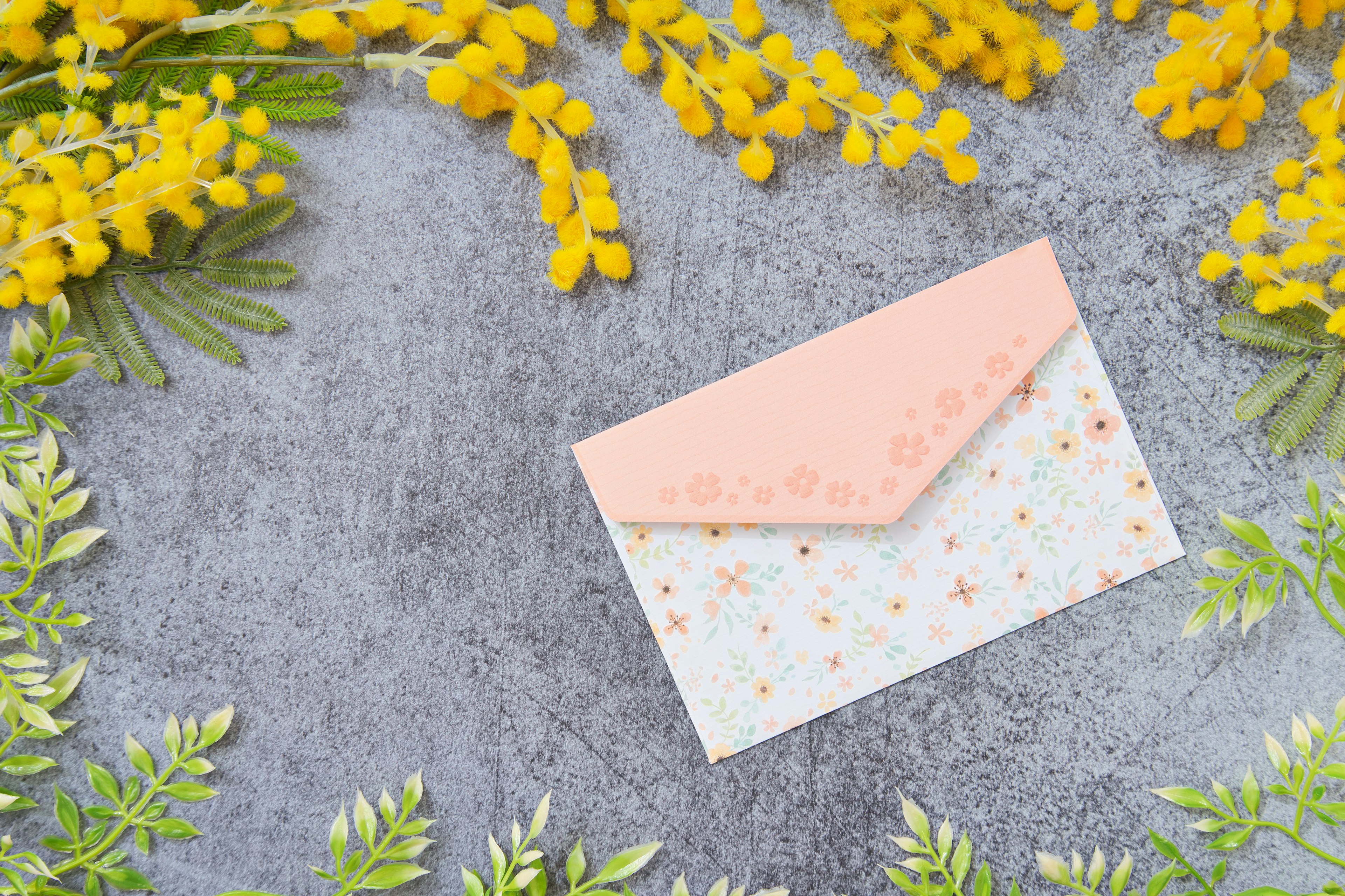 Pink envelope surrounded by yellow mimosa flowers and green leaves