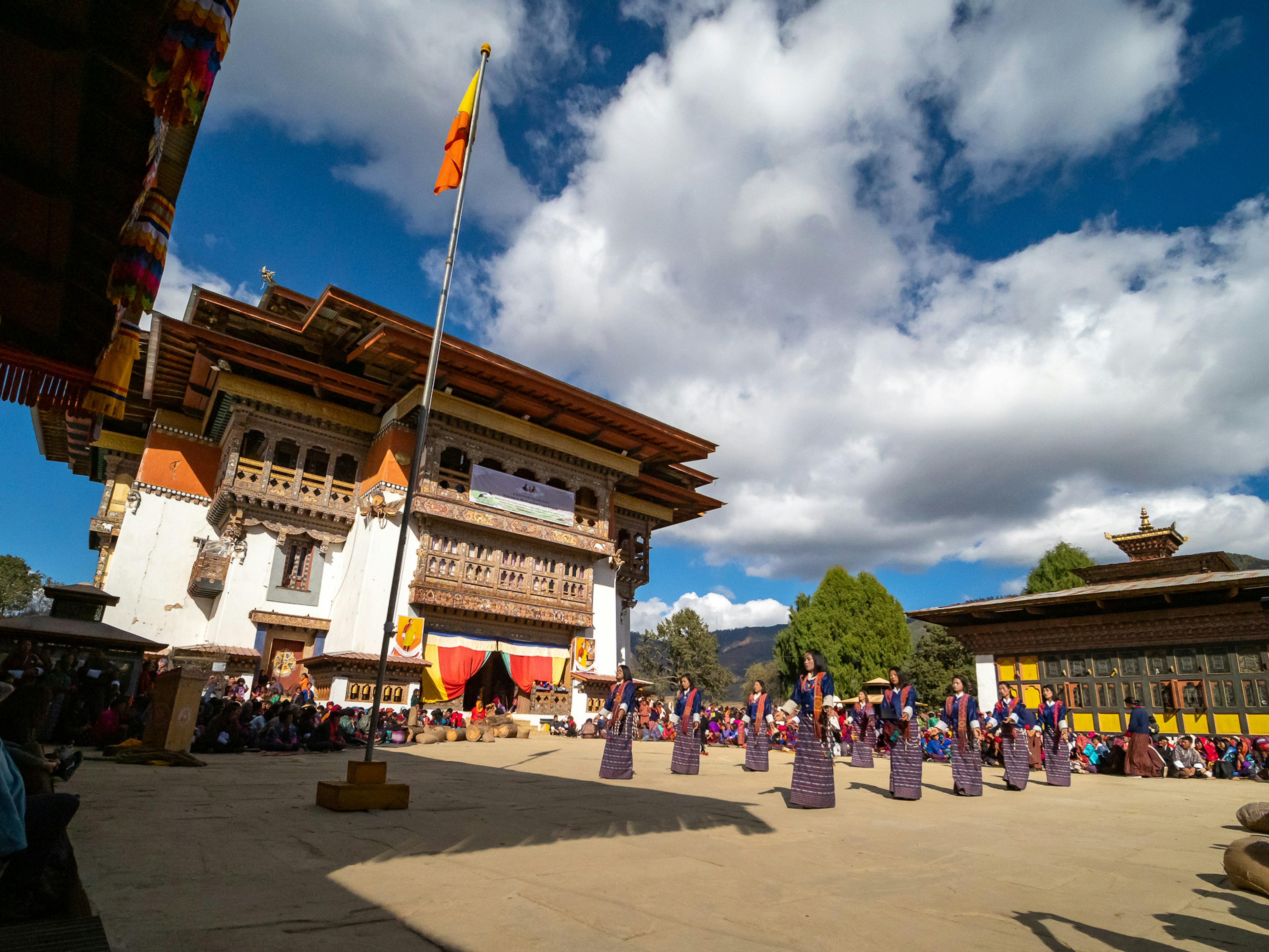 Un patio tradicional en Bután con bailarines en vestimenta tradicional bajo un hermoso cielo