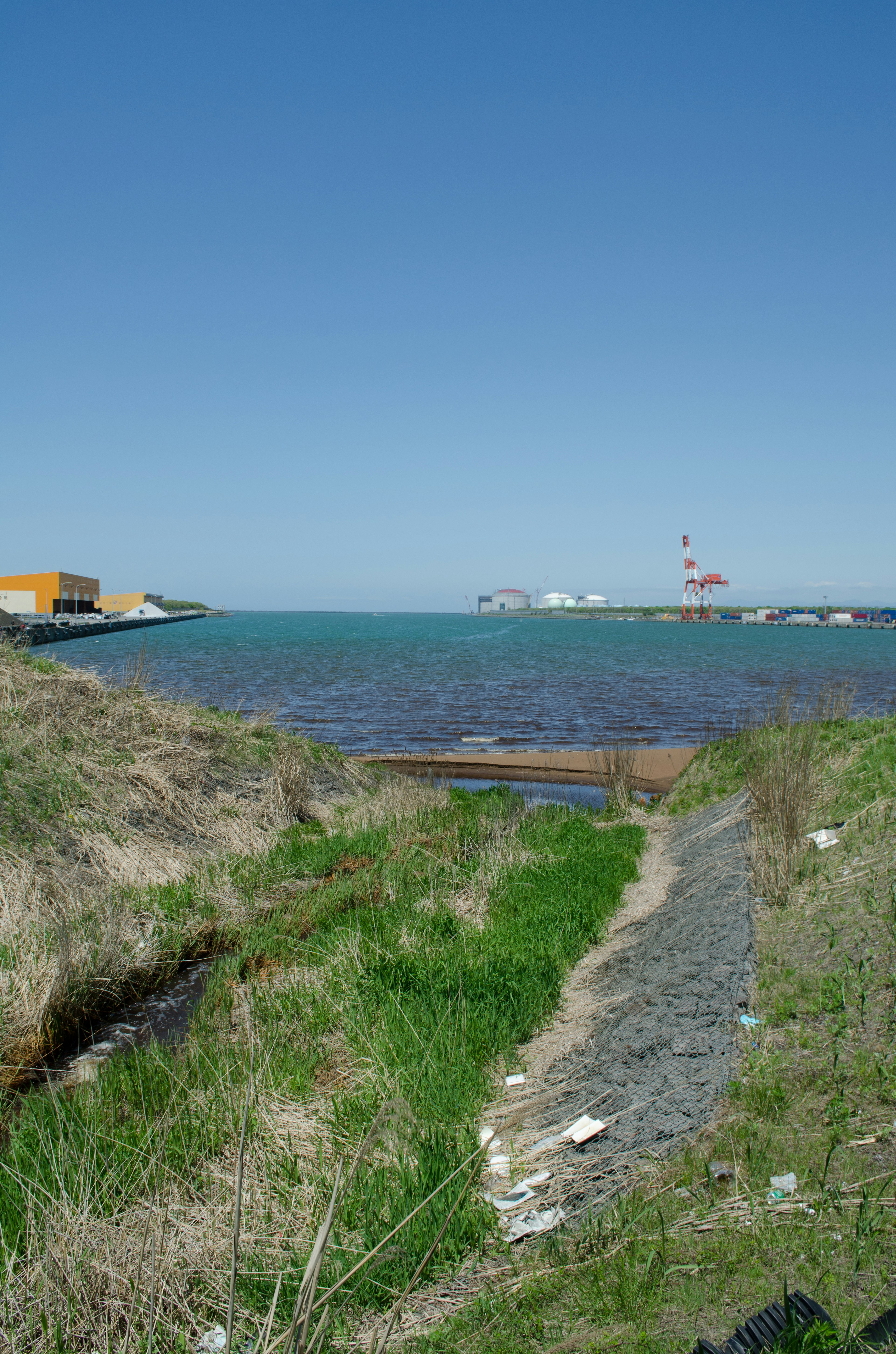 Scenic view of blue sea and sky with green grass and path visible harbor buildings in the background