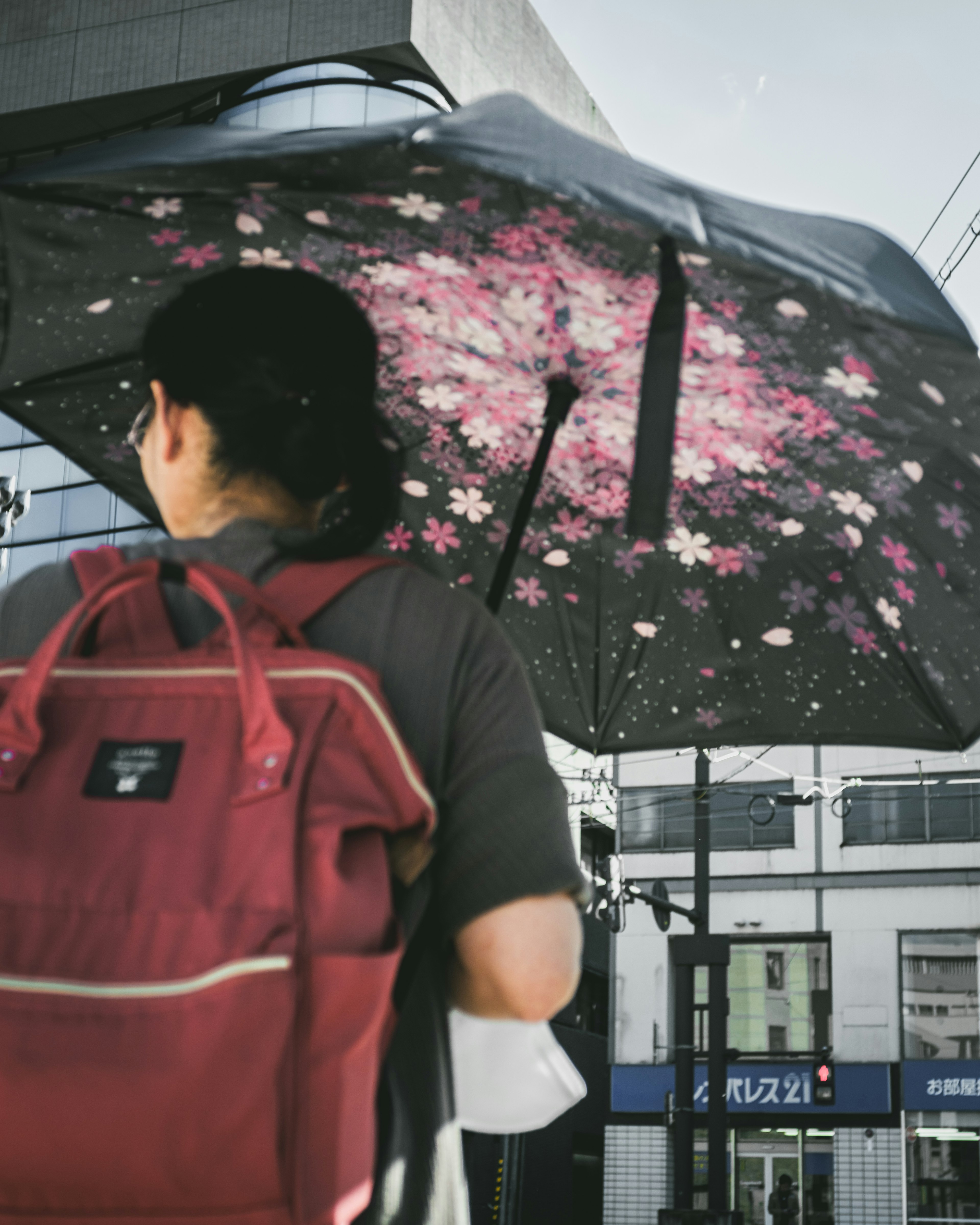 Person steht unter einem Regenschirm mit floralem Muster und trägt einen roten Rucksack