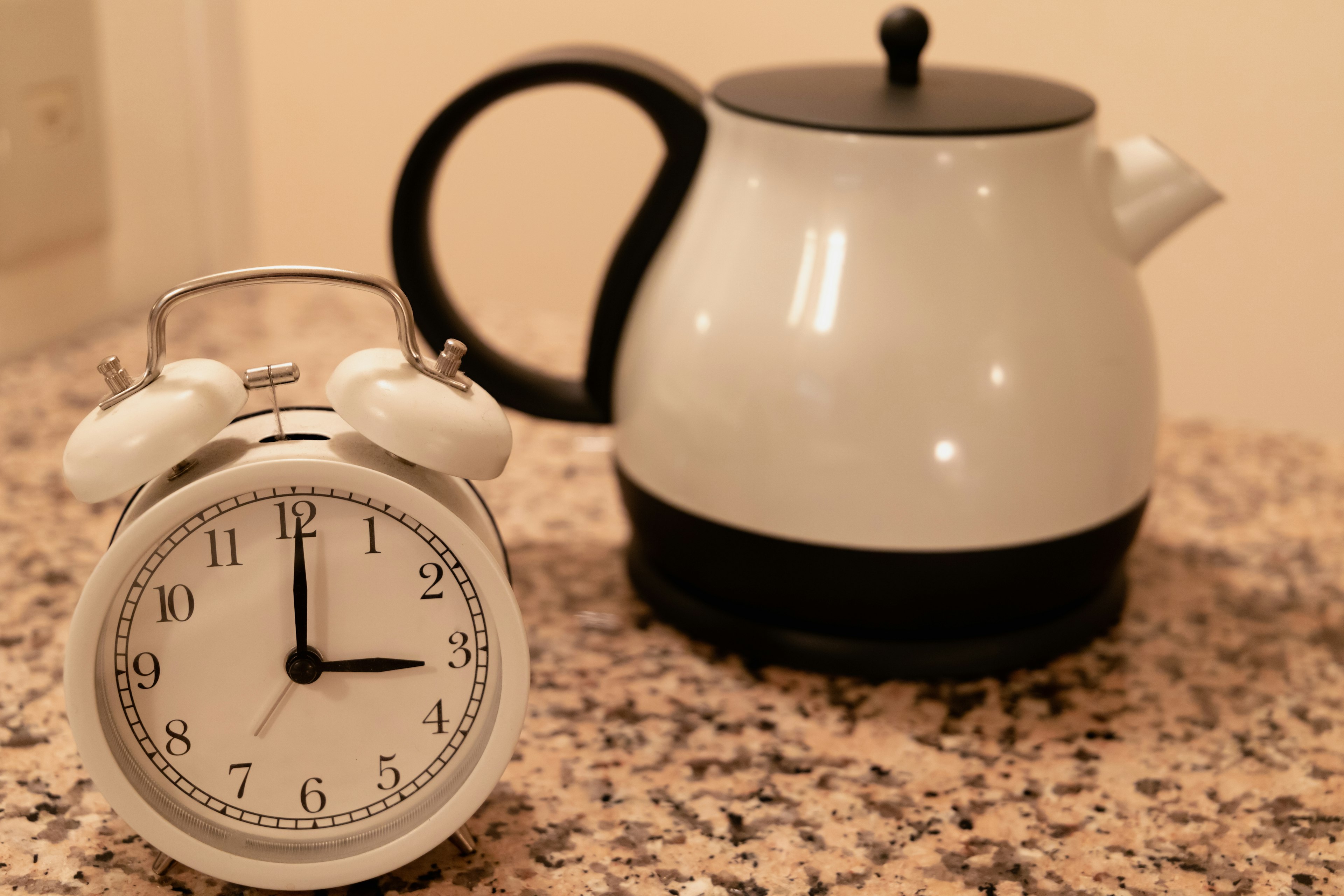 A white teapot and an alarm clock on a kitchen countertop