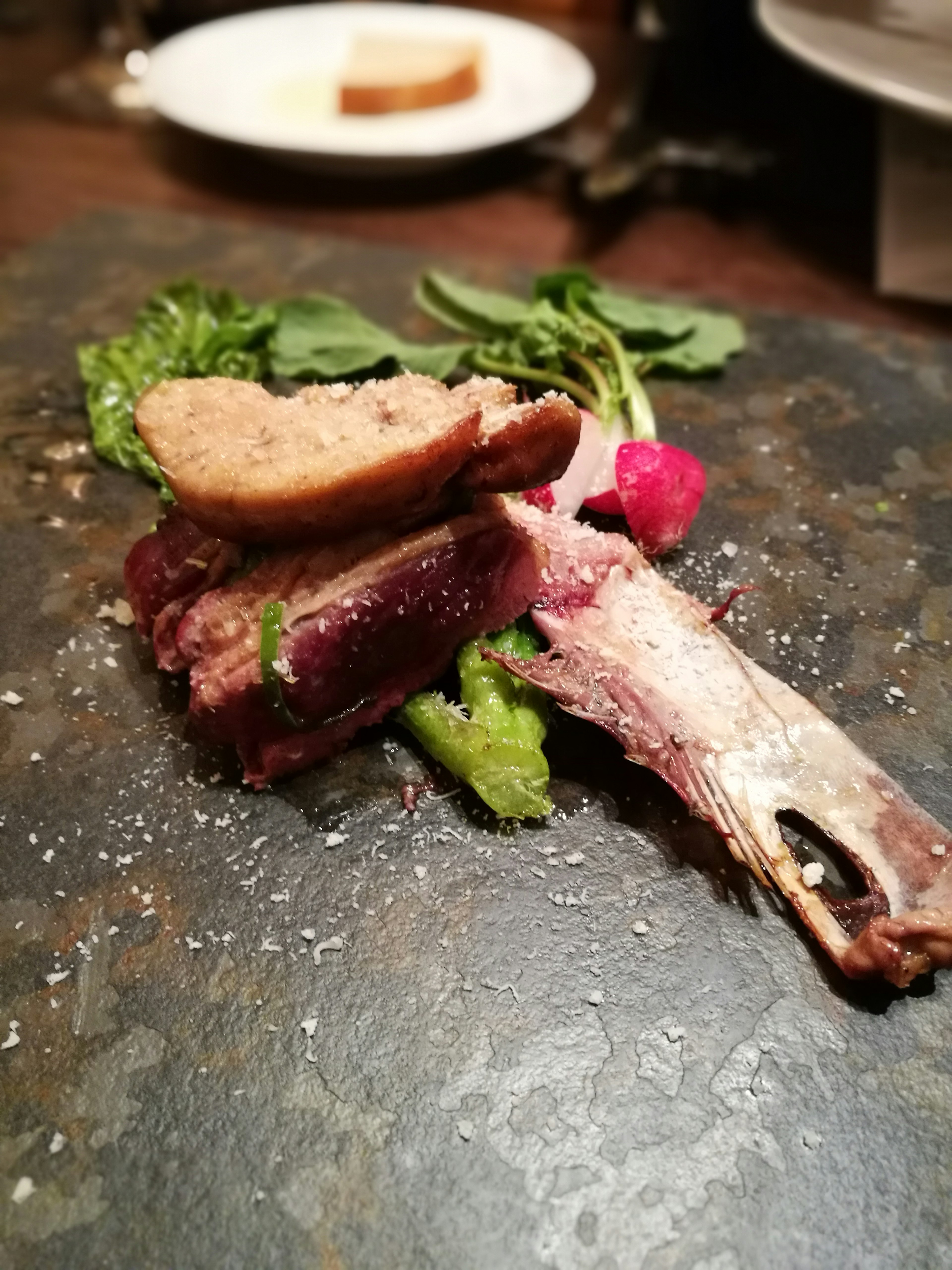 A beautifully plated dish featuring meat, greens, and a slice of bread