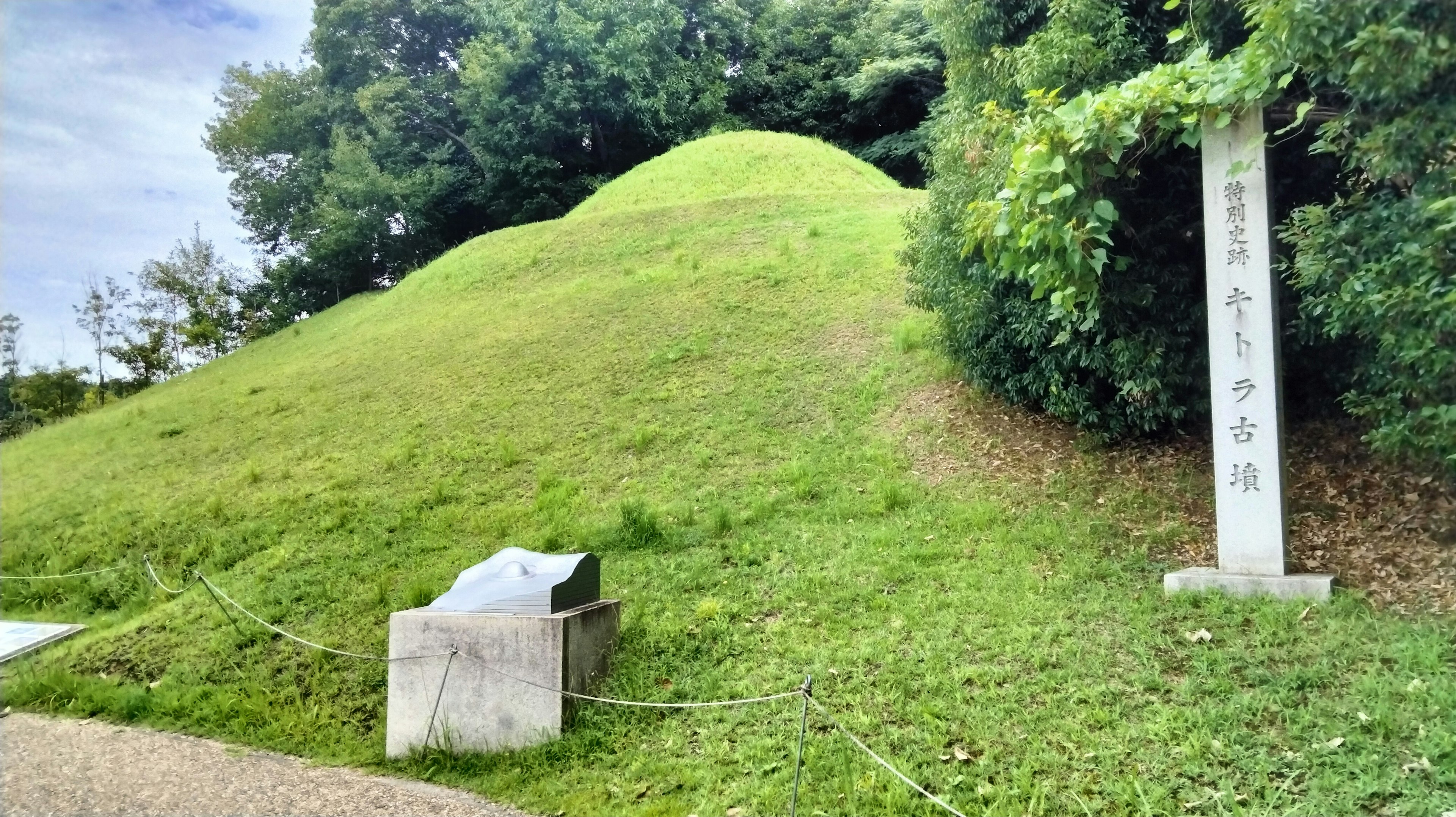 A small grassy mound with a stone marker nearby in a green landscape