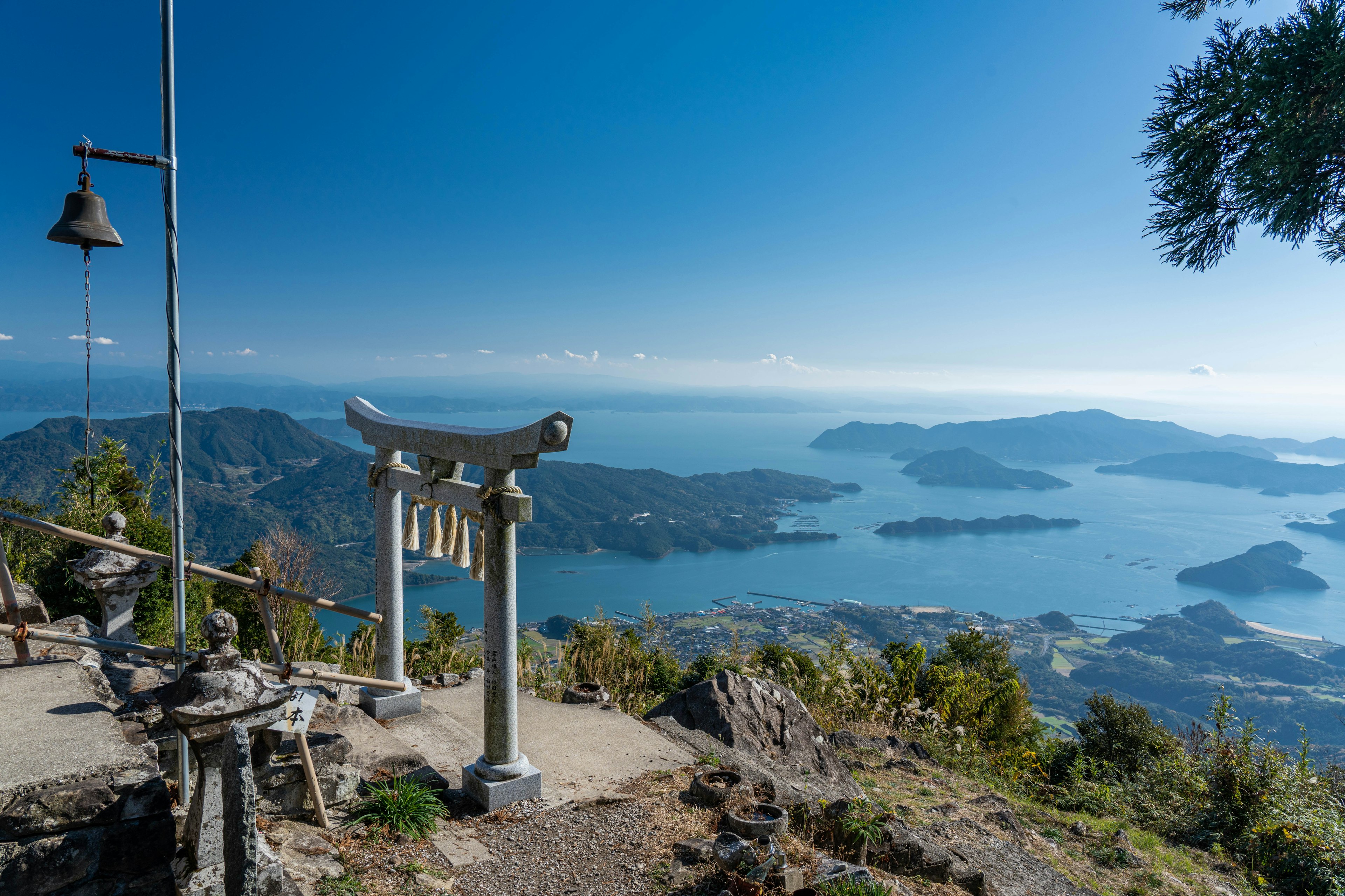 Torii e campana in cima a una montagna con vista su un bellissimo mare