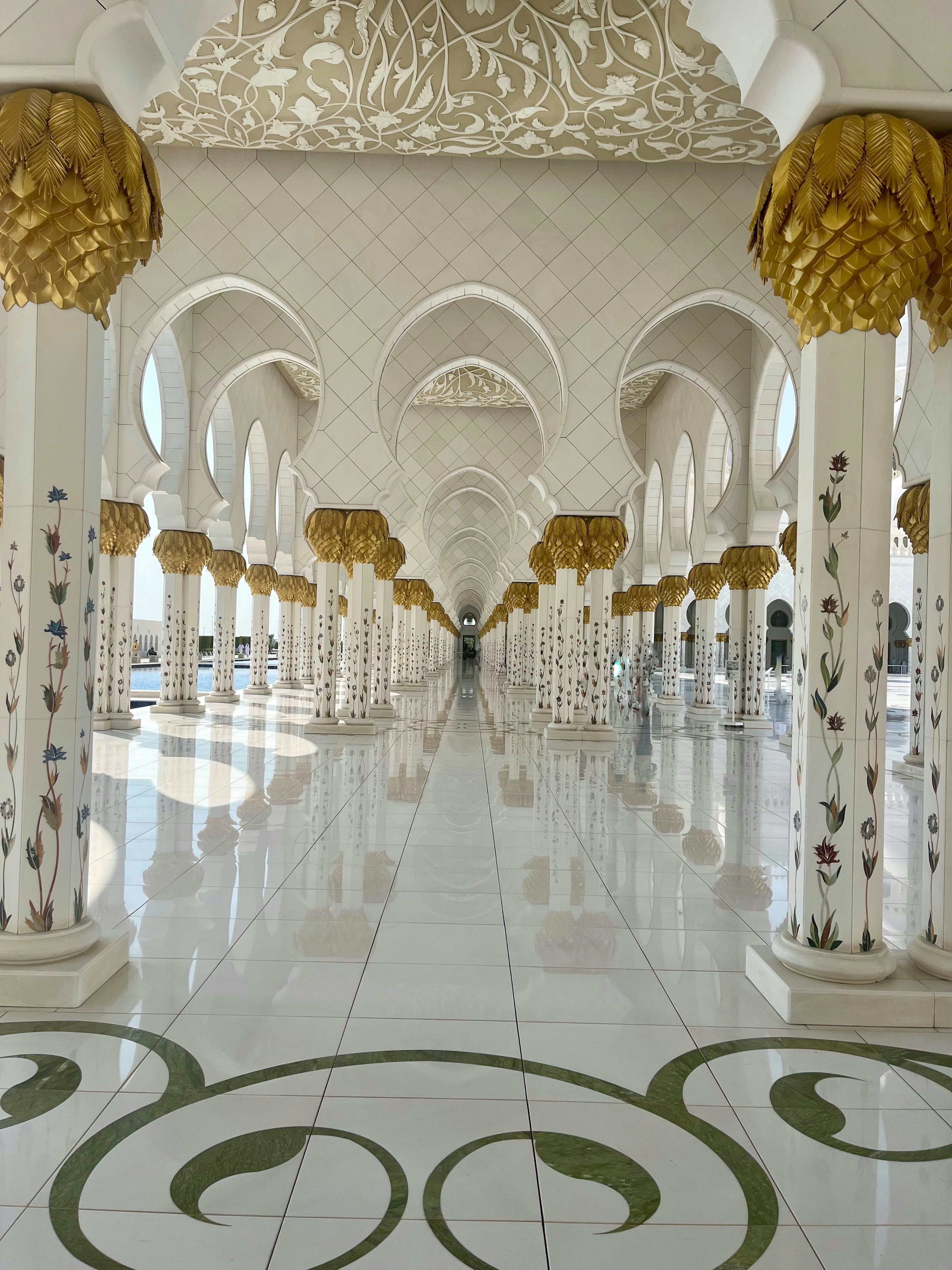 Interior corridor of a mosque featuring white marble columns and golden decorations