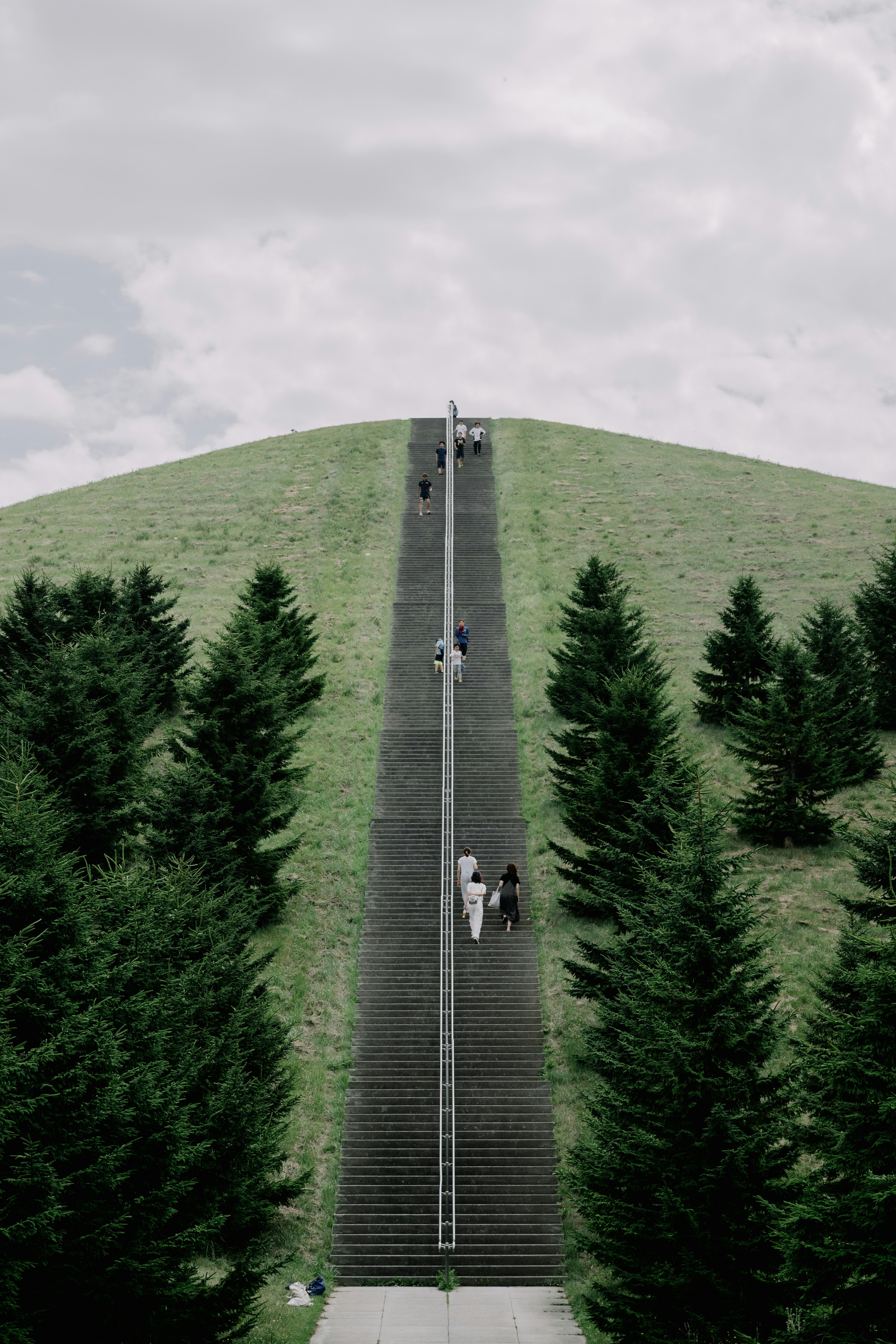 People ascending a long staircase on a green hill