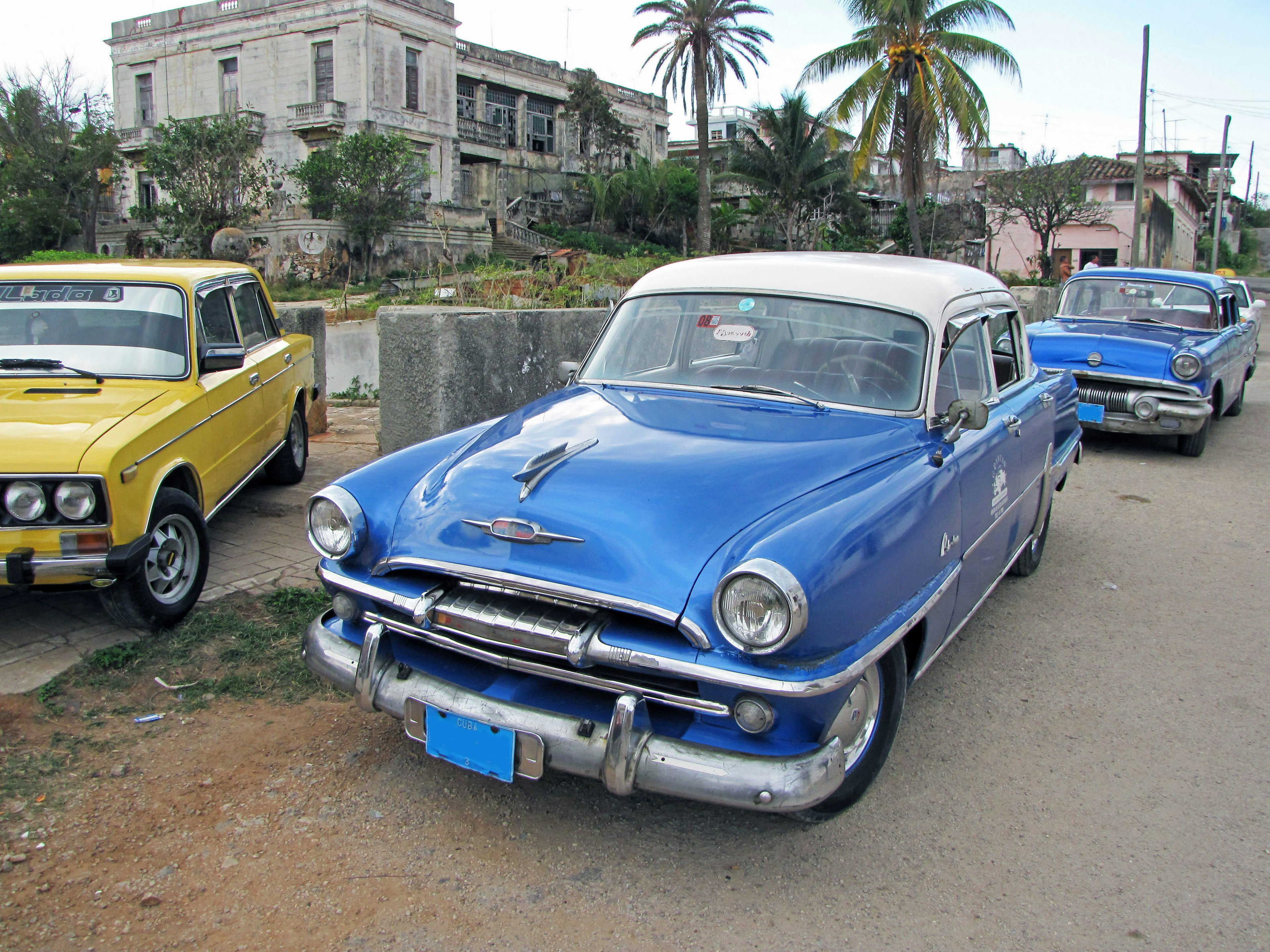 Klassisches blaues Auto neben Vintage-Fahrzeugen und alten Gebäuden geparkt