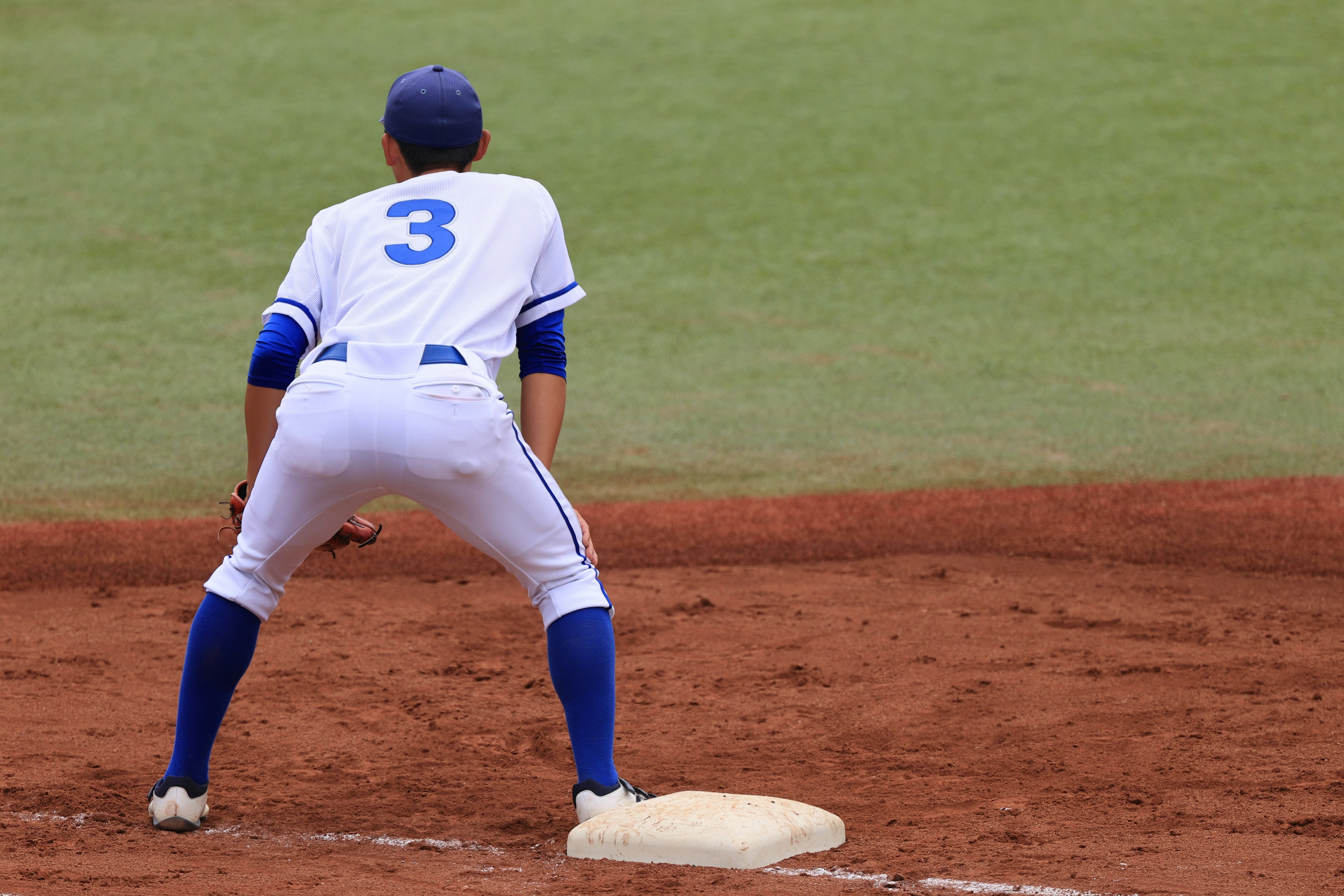 Jugador de béisbol en uniforme blanco y calcetas azules posicionado en la primera base