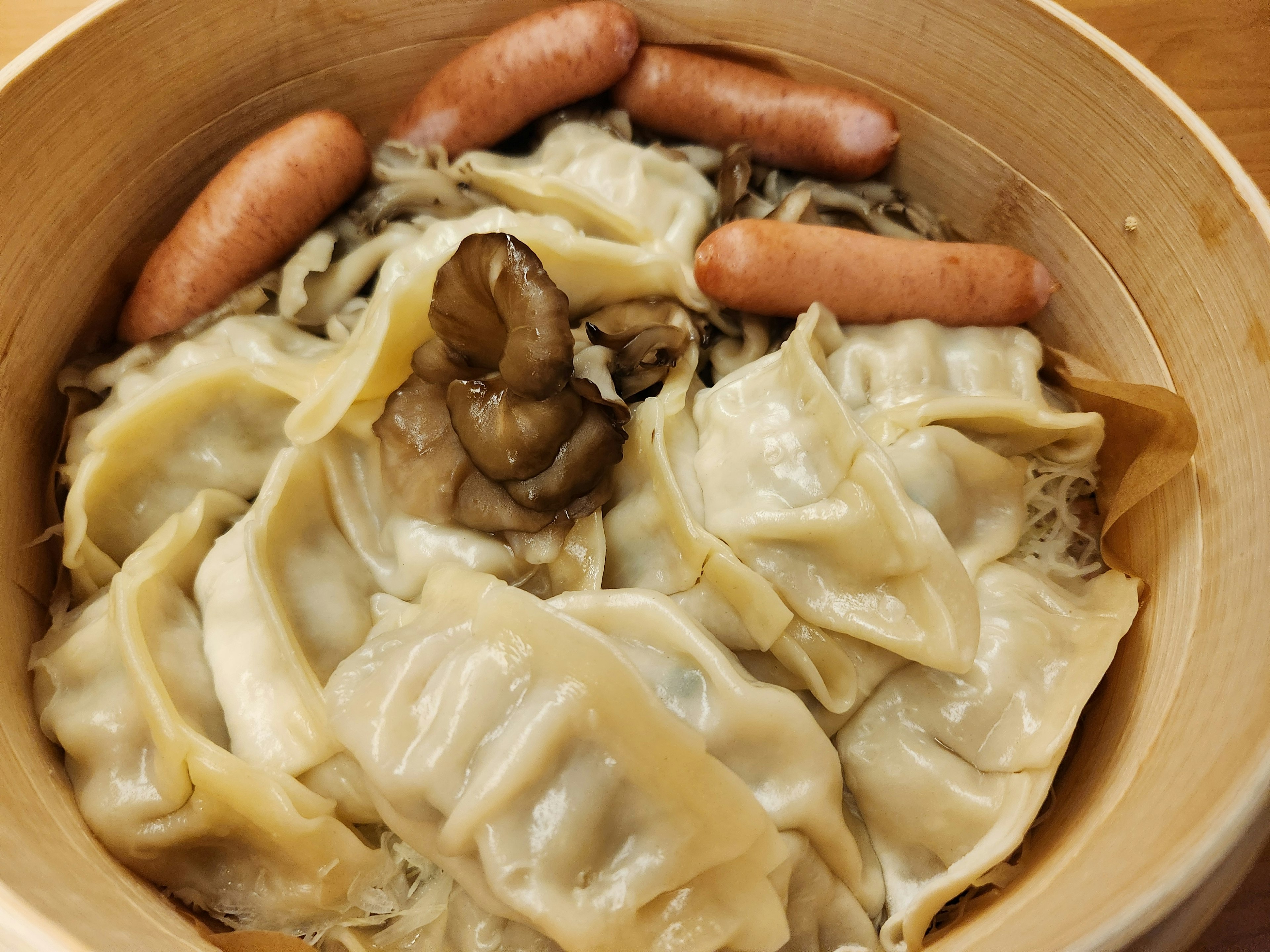 Dumplings cuits à la vapeur et saucisses disposés dans un cuiseur vapeur en bambou