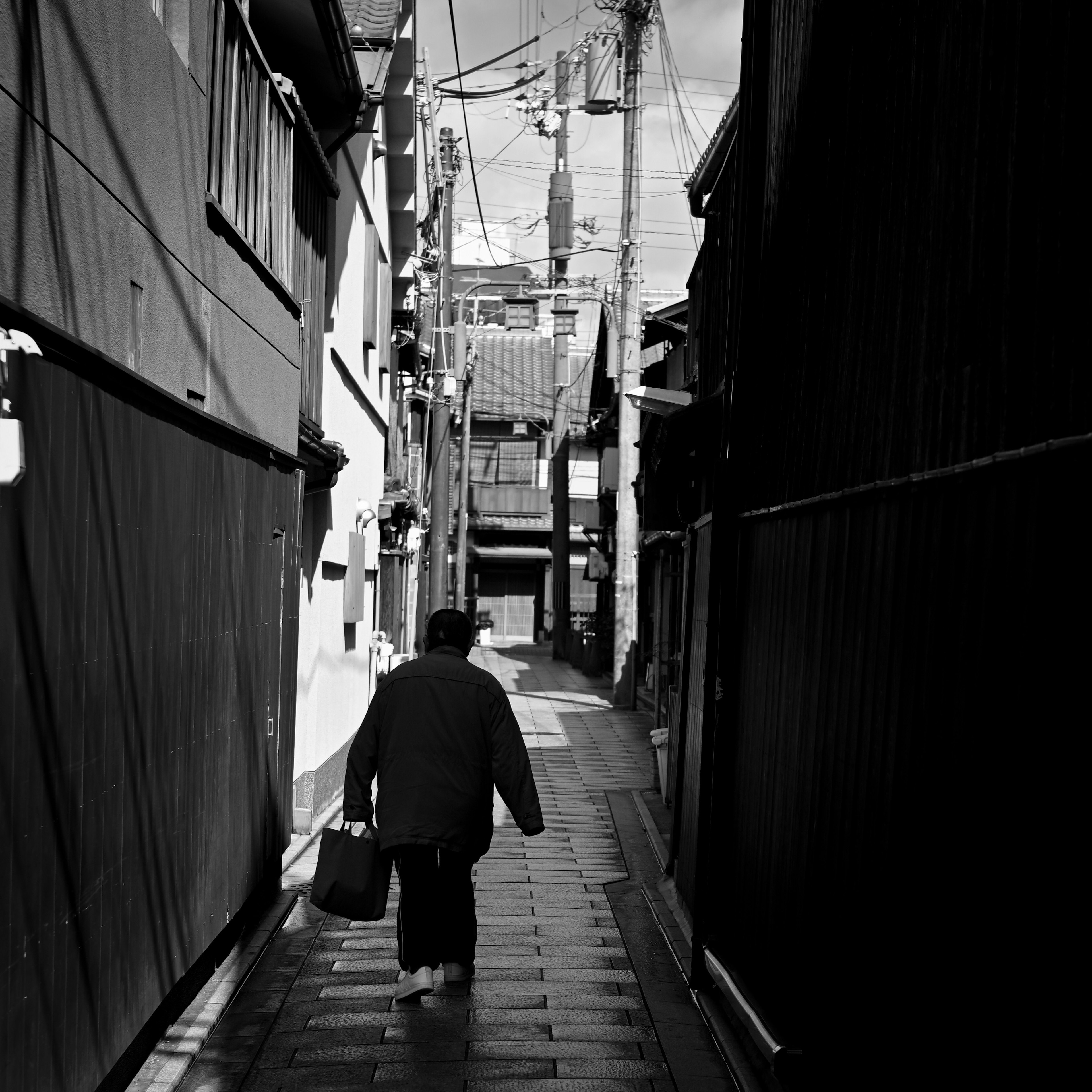 Foto hitam putih seorang pria berpakaian kimono berjalan di gang sempit