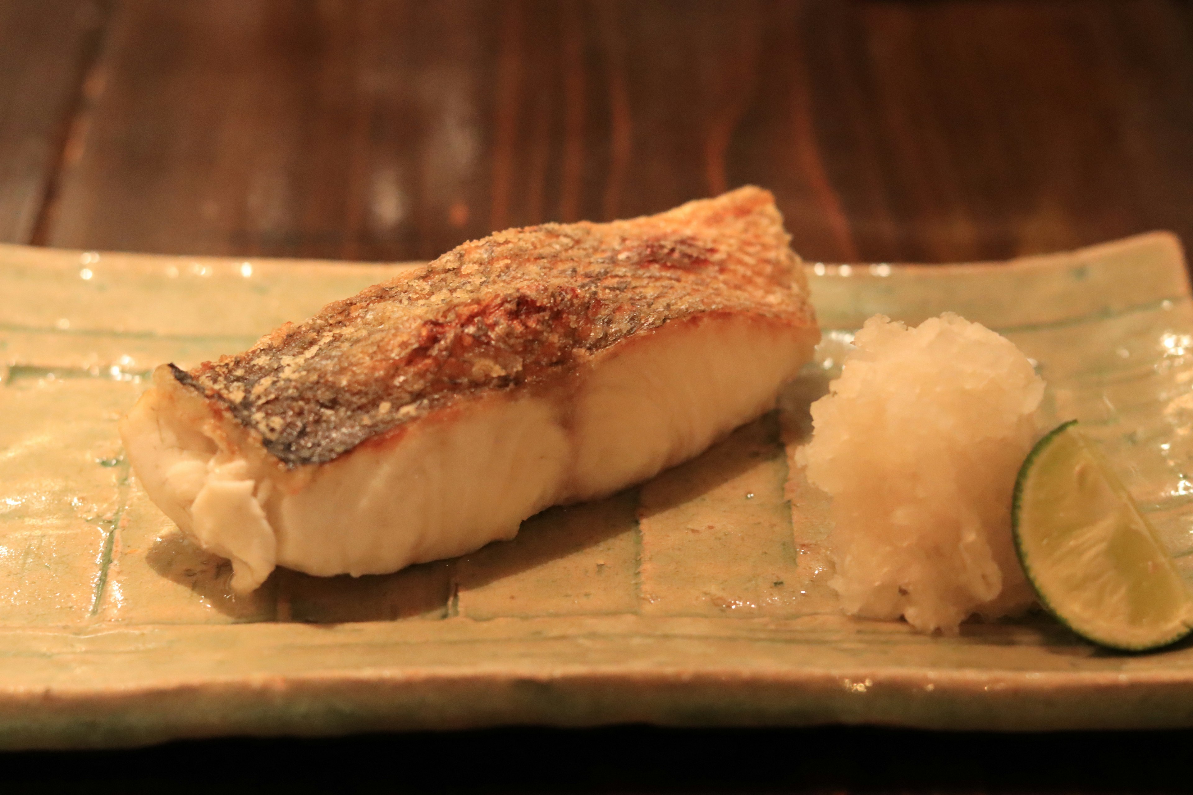 Gegrillter Fisch serviert mit geriebenem Daikon und einer Limettenscheibe auf einem traditionellen japanischen Teller