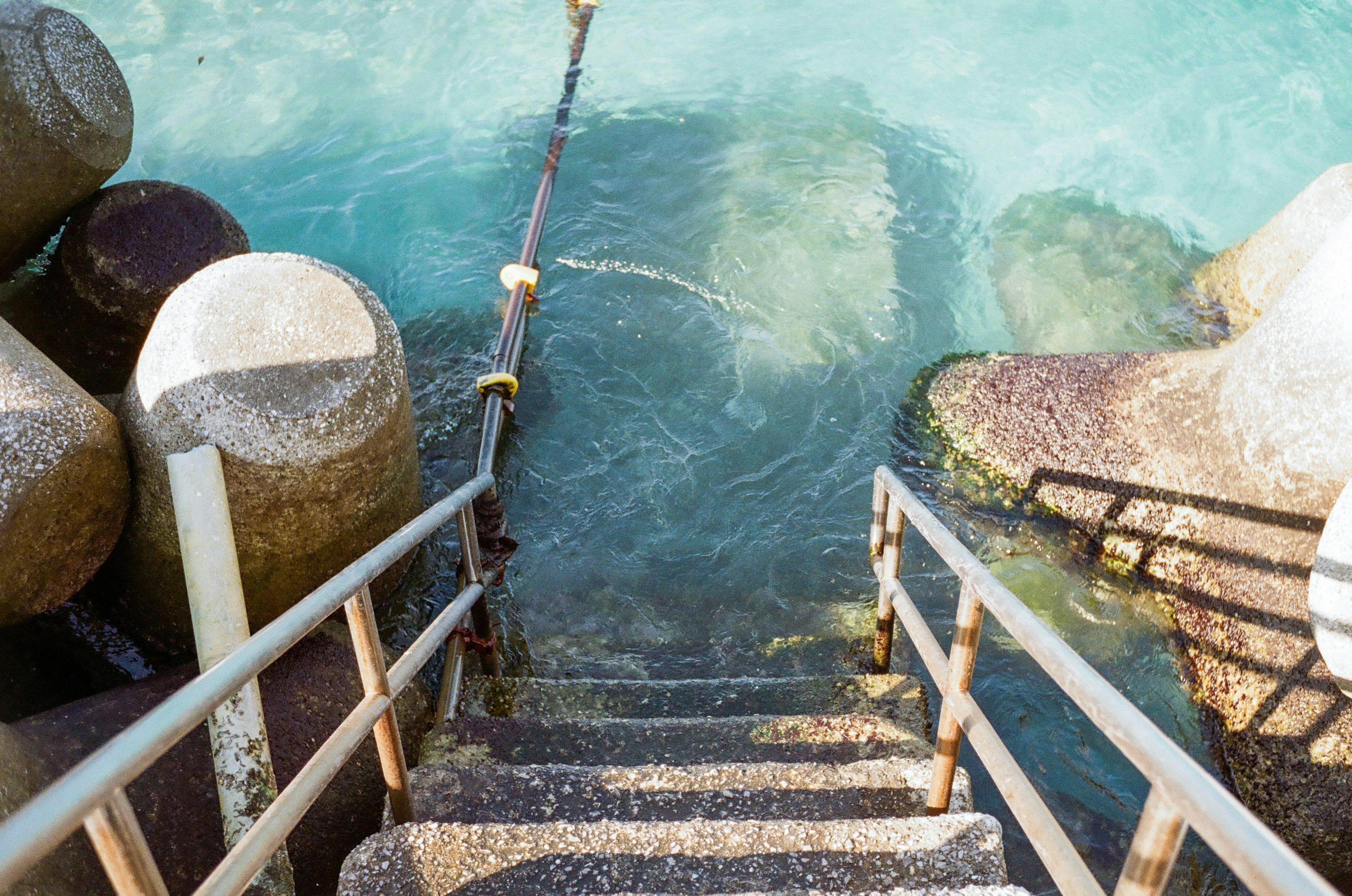 Treppe, die ins klare Wasser führt, mit Betonblöcken in der Nähe