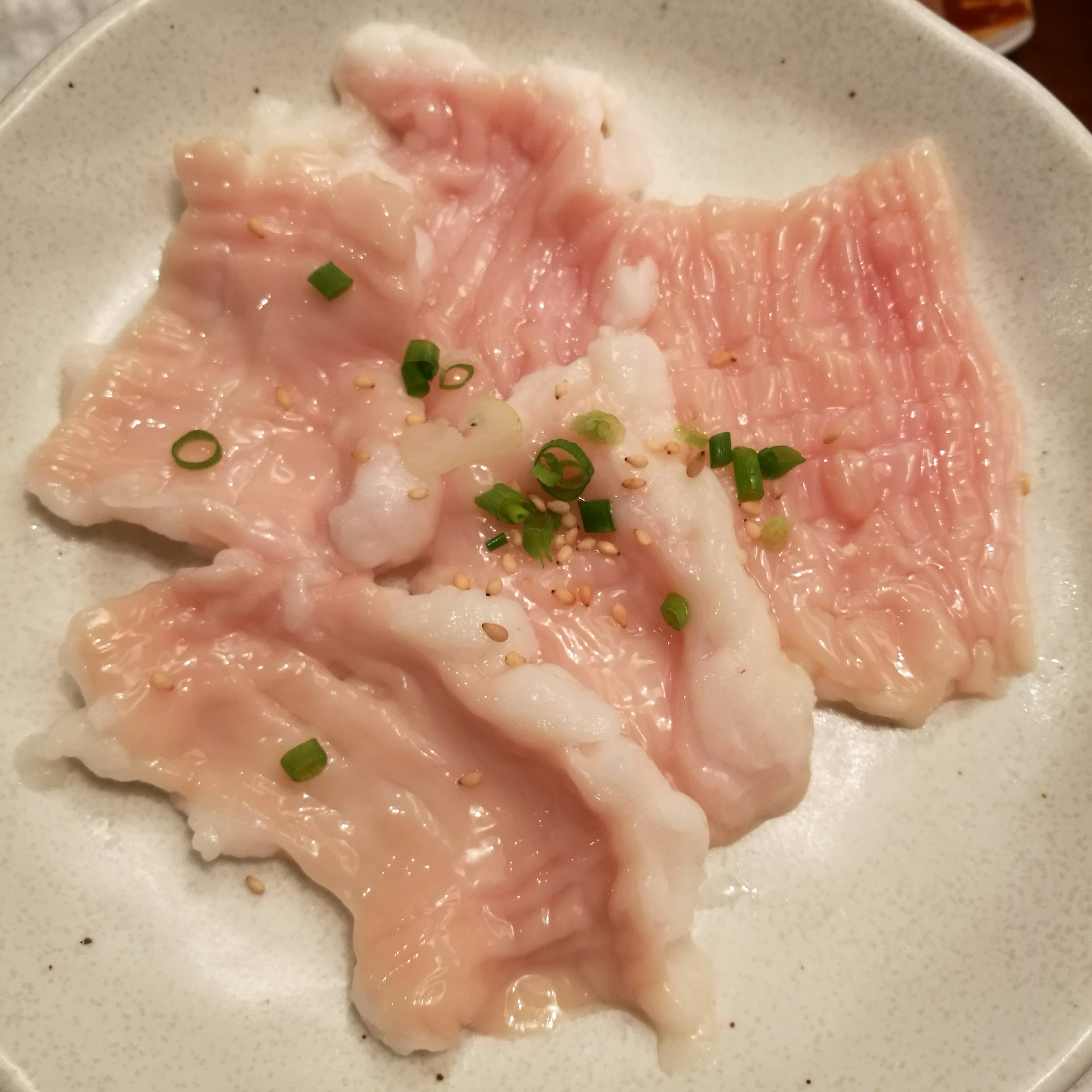 Carne en rodajas finas dispuesta en un plato blanco decorada con cebollitas verdes y semillas de sésamo