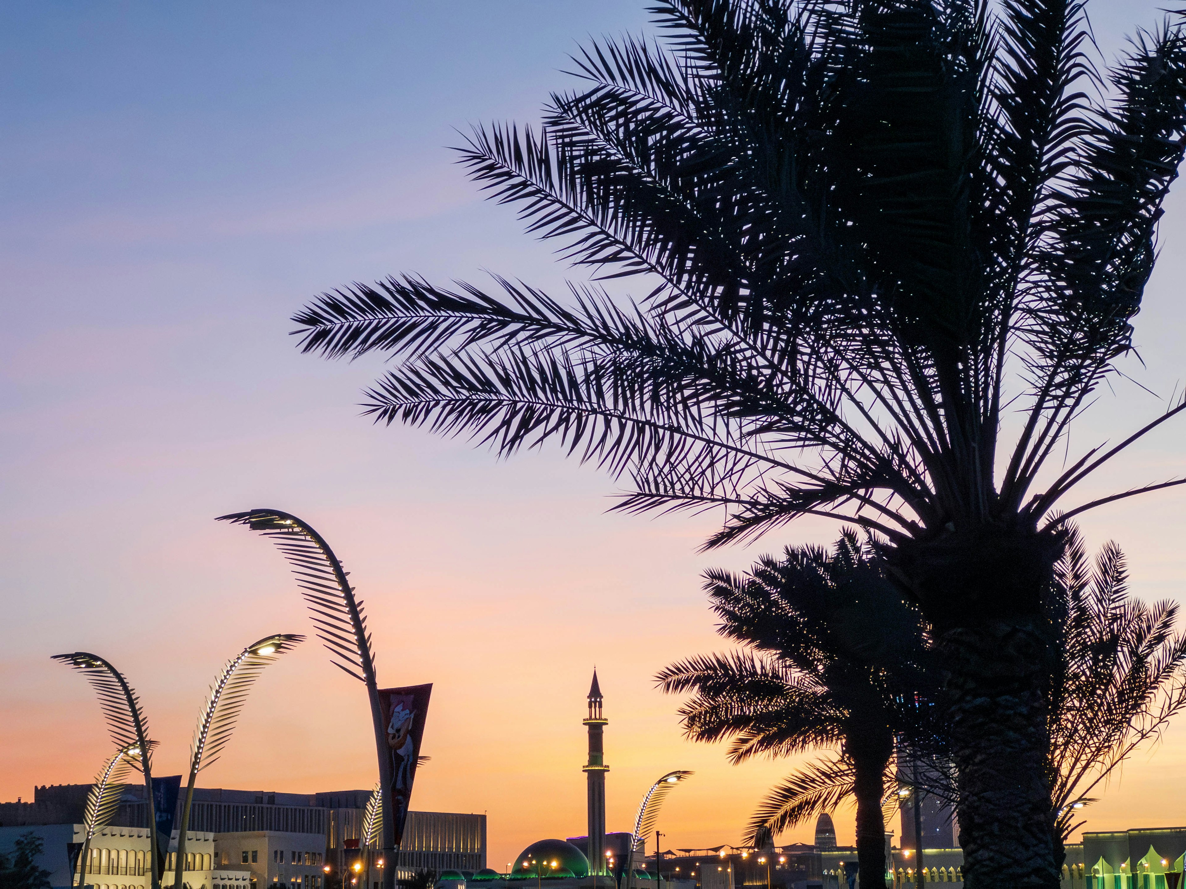 Silhouette of palm trees against a sunset sky with a mosque minaret