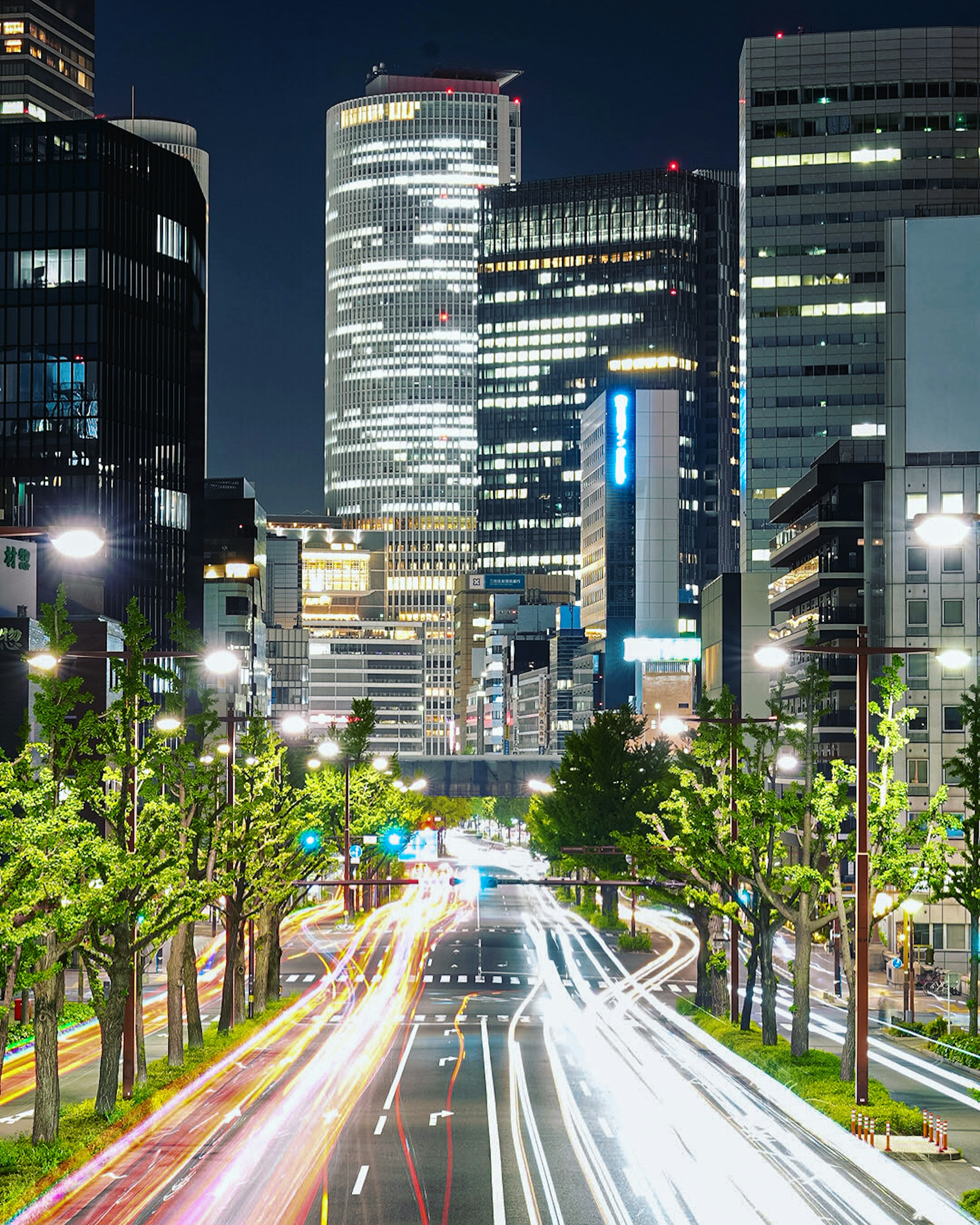 夜の都市の風景 高層ビルと明るい街灯が並ぶ通り 車のライトが流れるように写っている