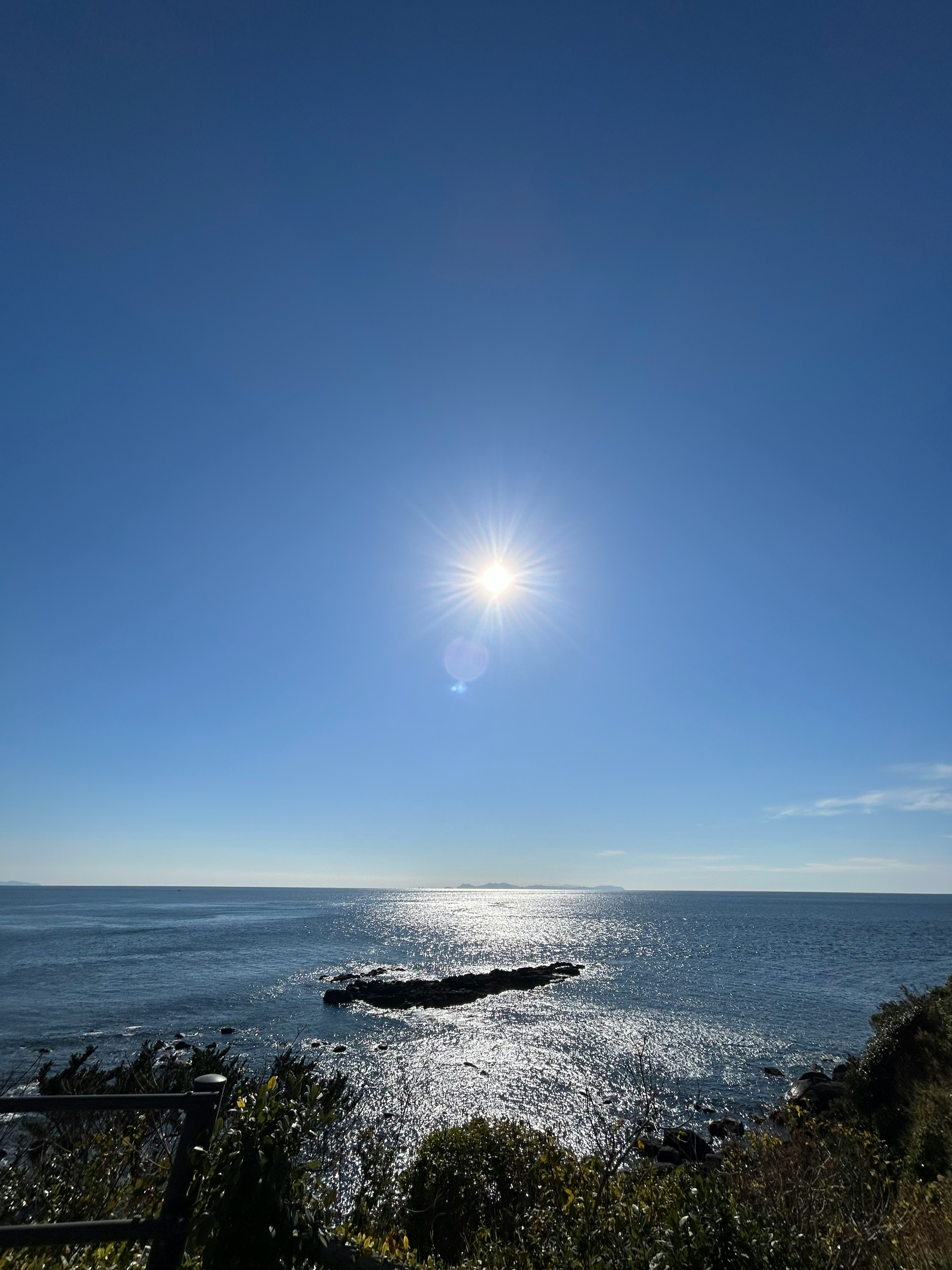 明亮的太陽照耀在平靜的藍色海洋和岩石海岸上