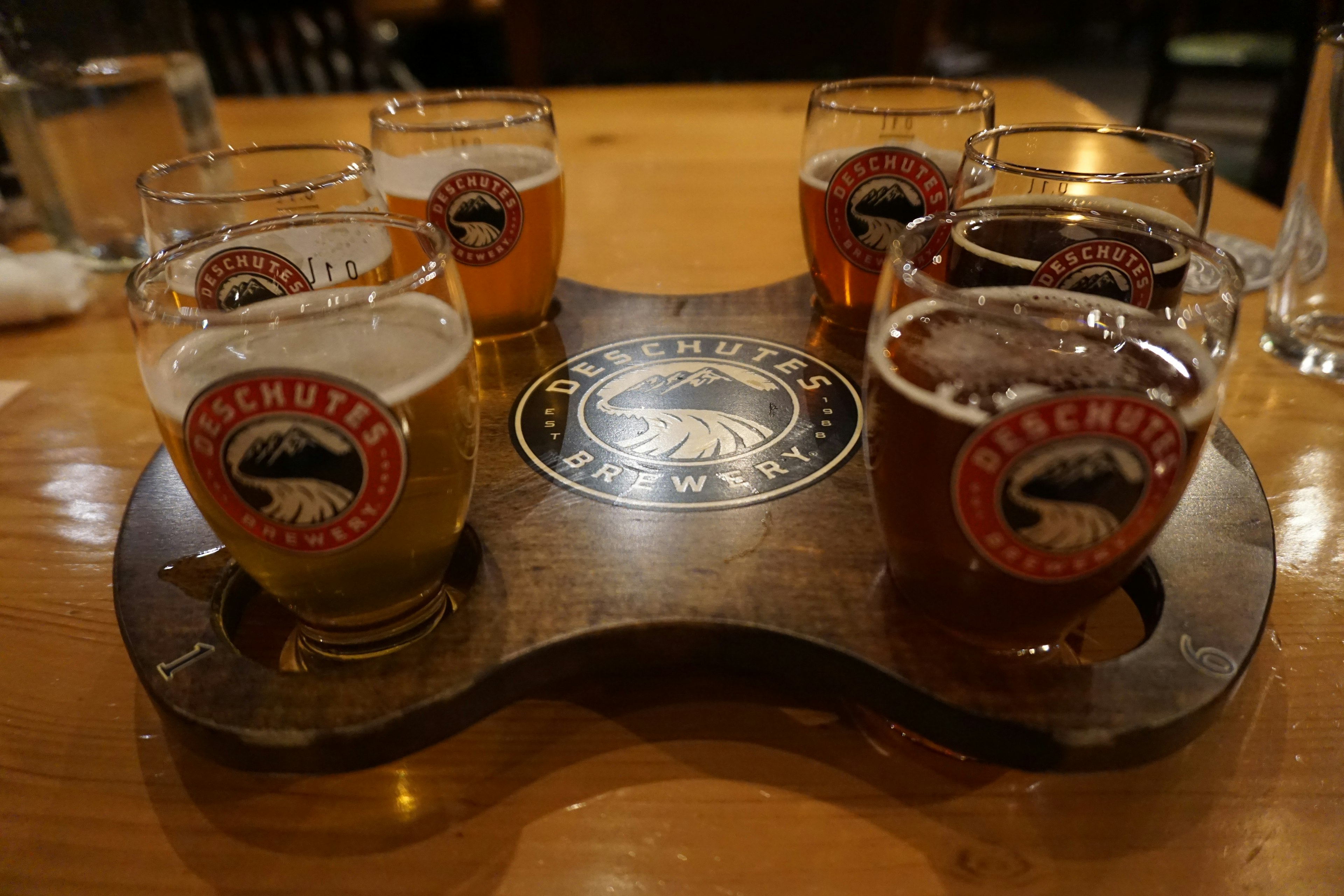 A wooden flight board holding multiple craft beer tasting glasses