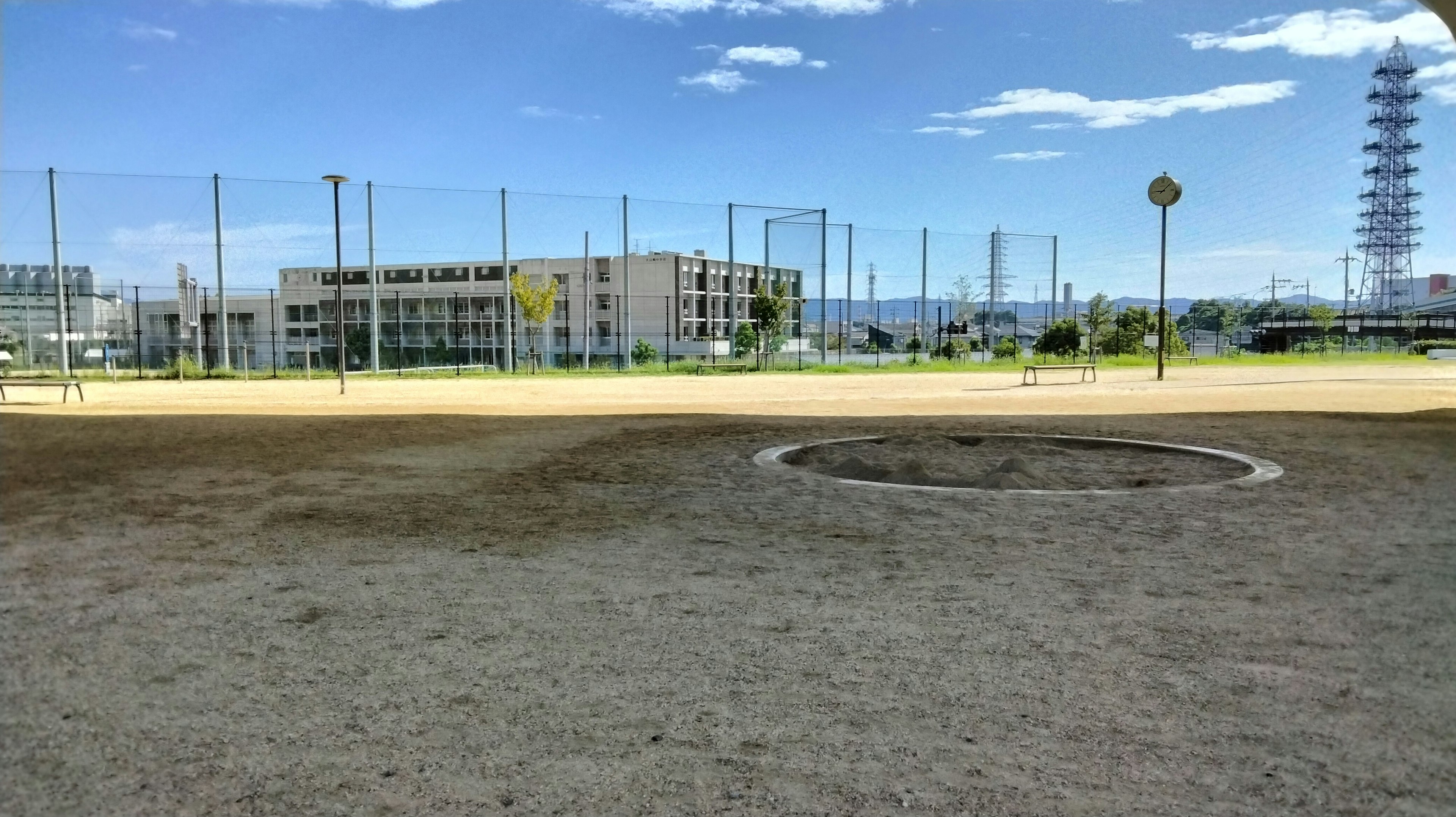 Breiter Sandbereich eines Parks unter blauem Himmel mit Gebäuden und Netzen