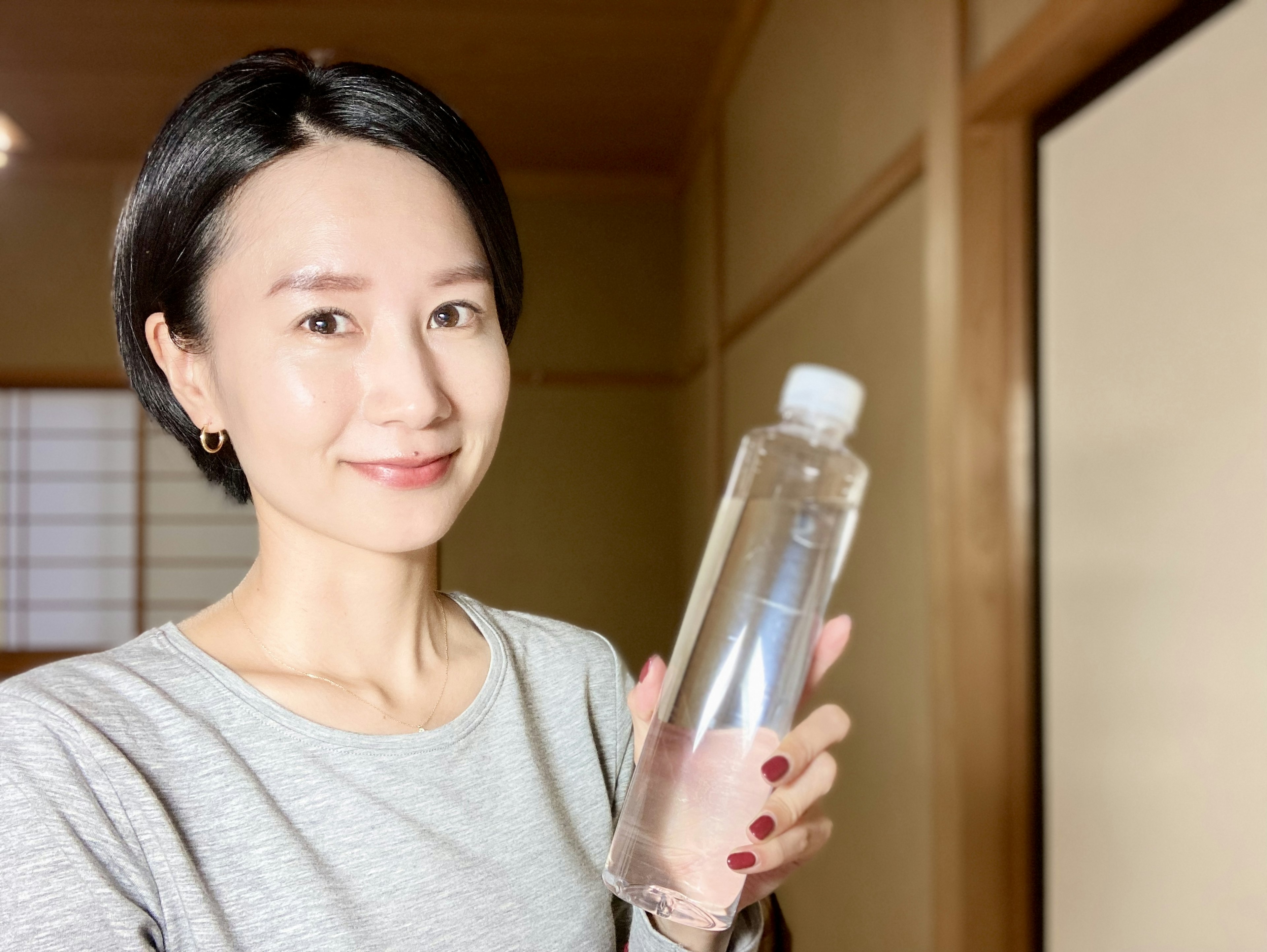 Wanita tersenyum sambil memegang botol bening di ruangan Jepang tradisional