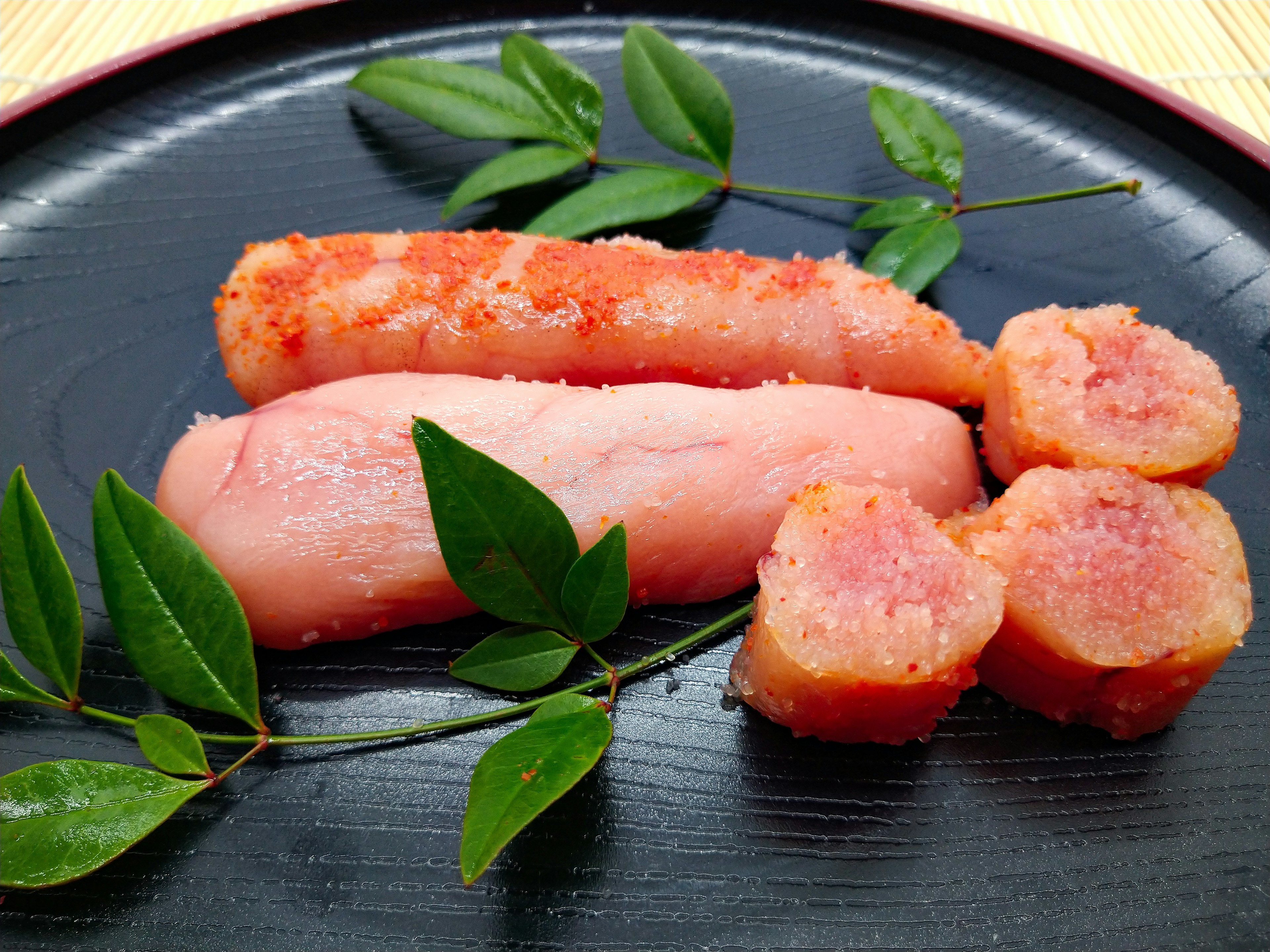 Vibrant fish roe arranged with green leaves on a black plate