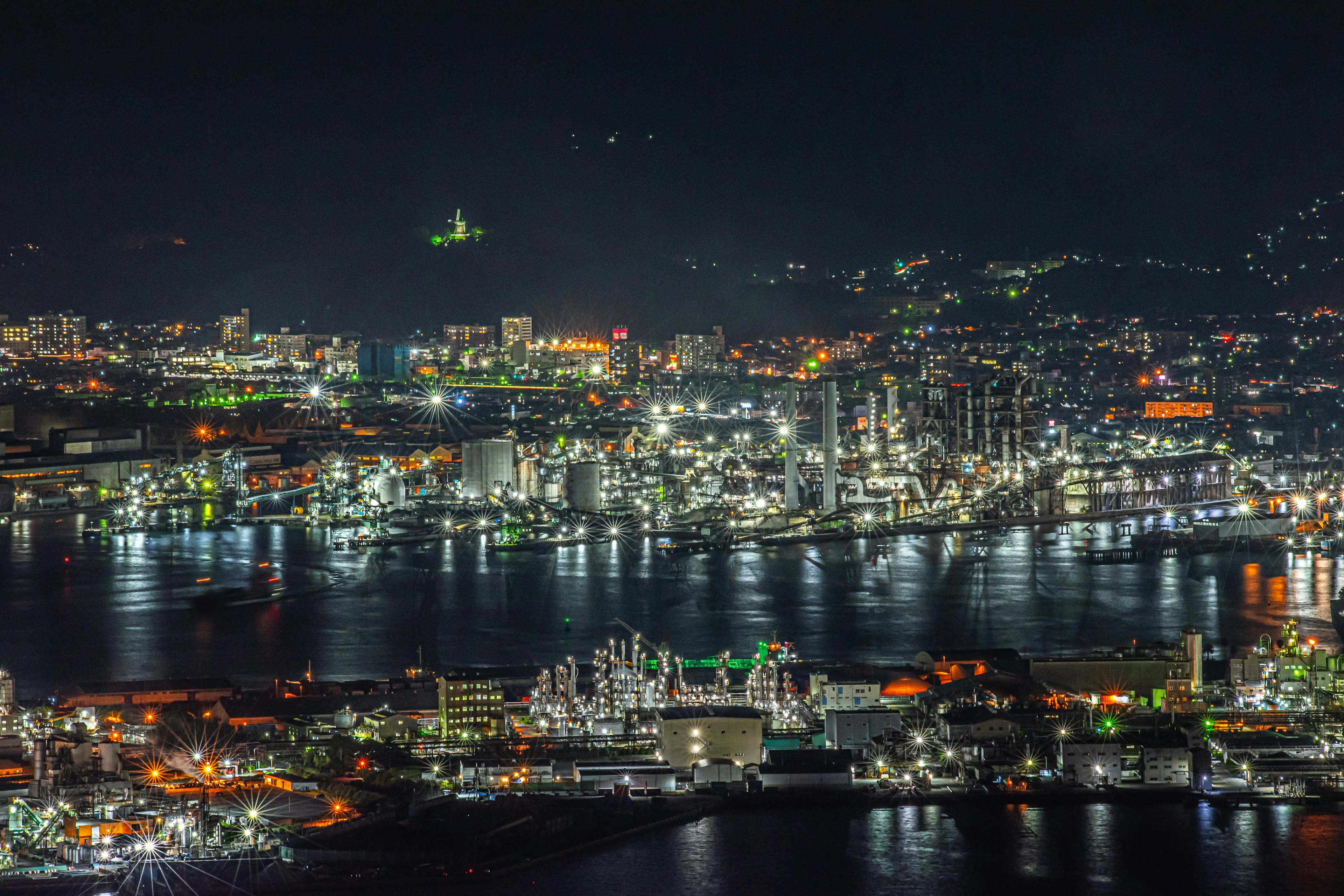 Illuminated industrial area of a port city at night with sparkling buildings and water surface