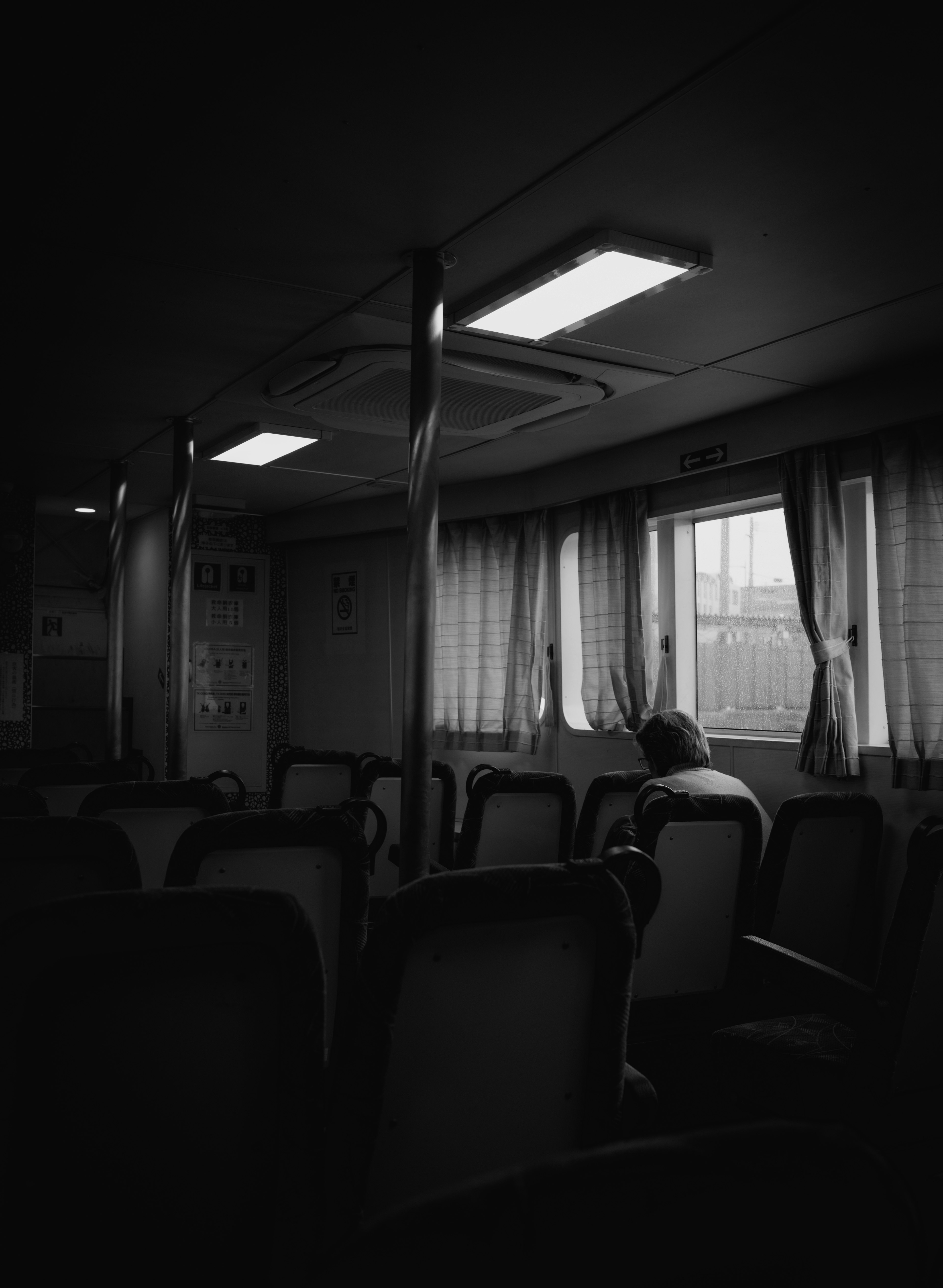 Silhouette of a person sitting in a dimly lit interior of a ferry Soft light from the window and curtain details