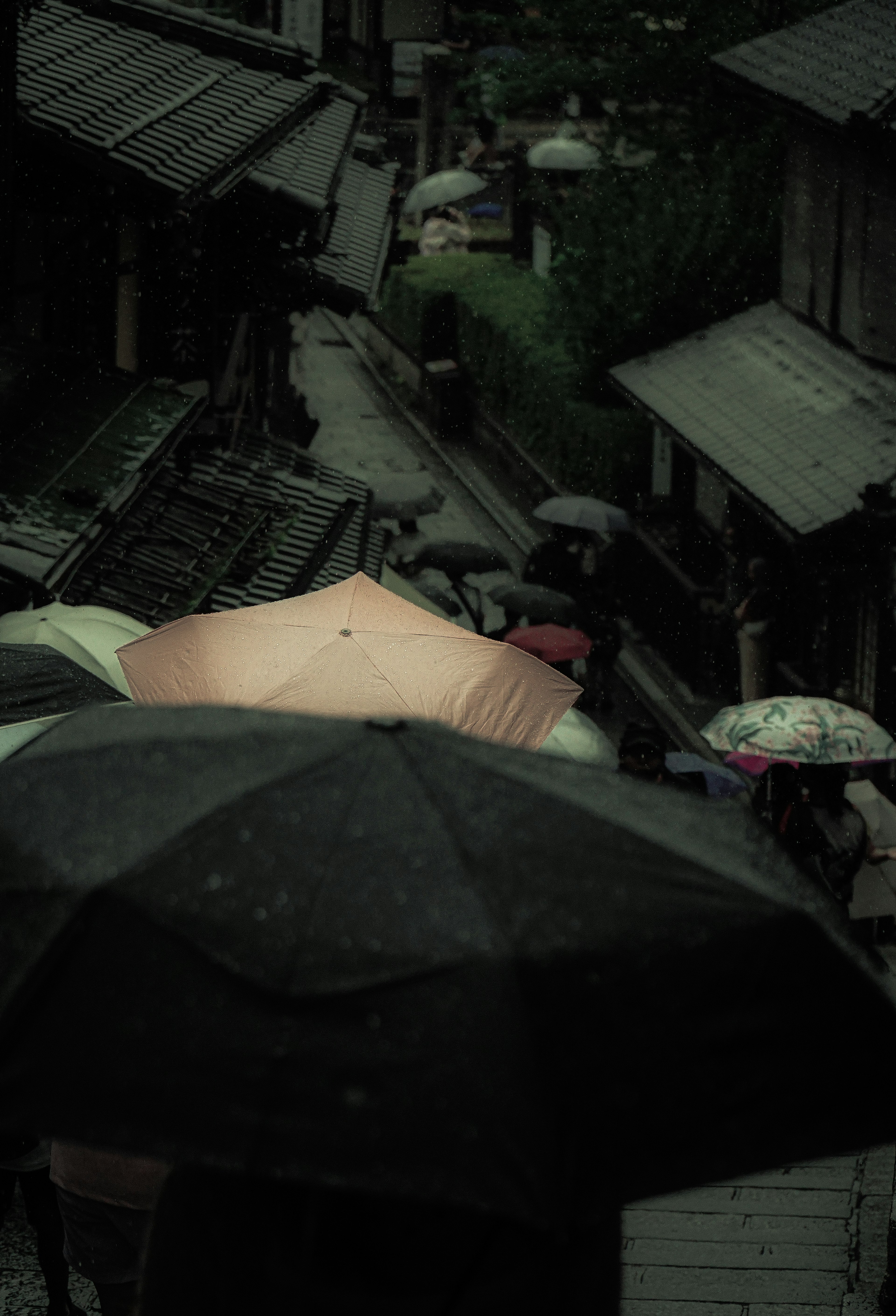 A scene of people walking with umbrellas in the rain A light umbrella stands out against a dark background